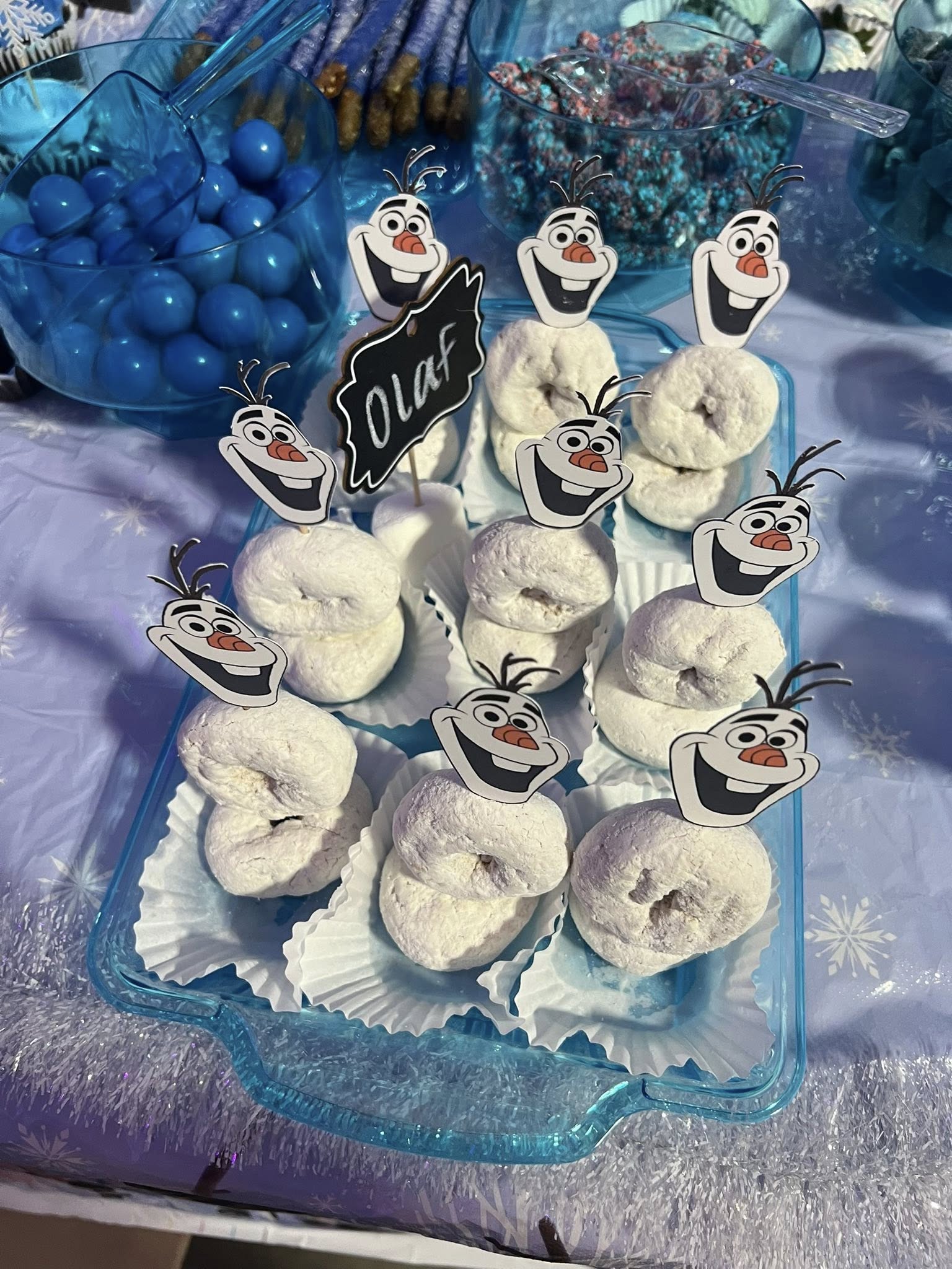 Snowman-themed donuts stacked with Olaf cupcake toppers on a blue tray