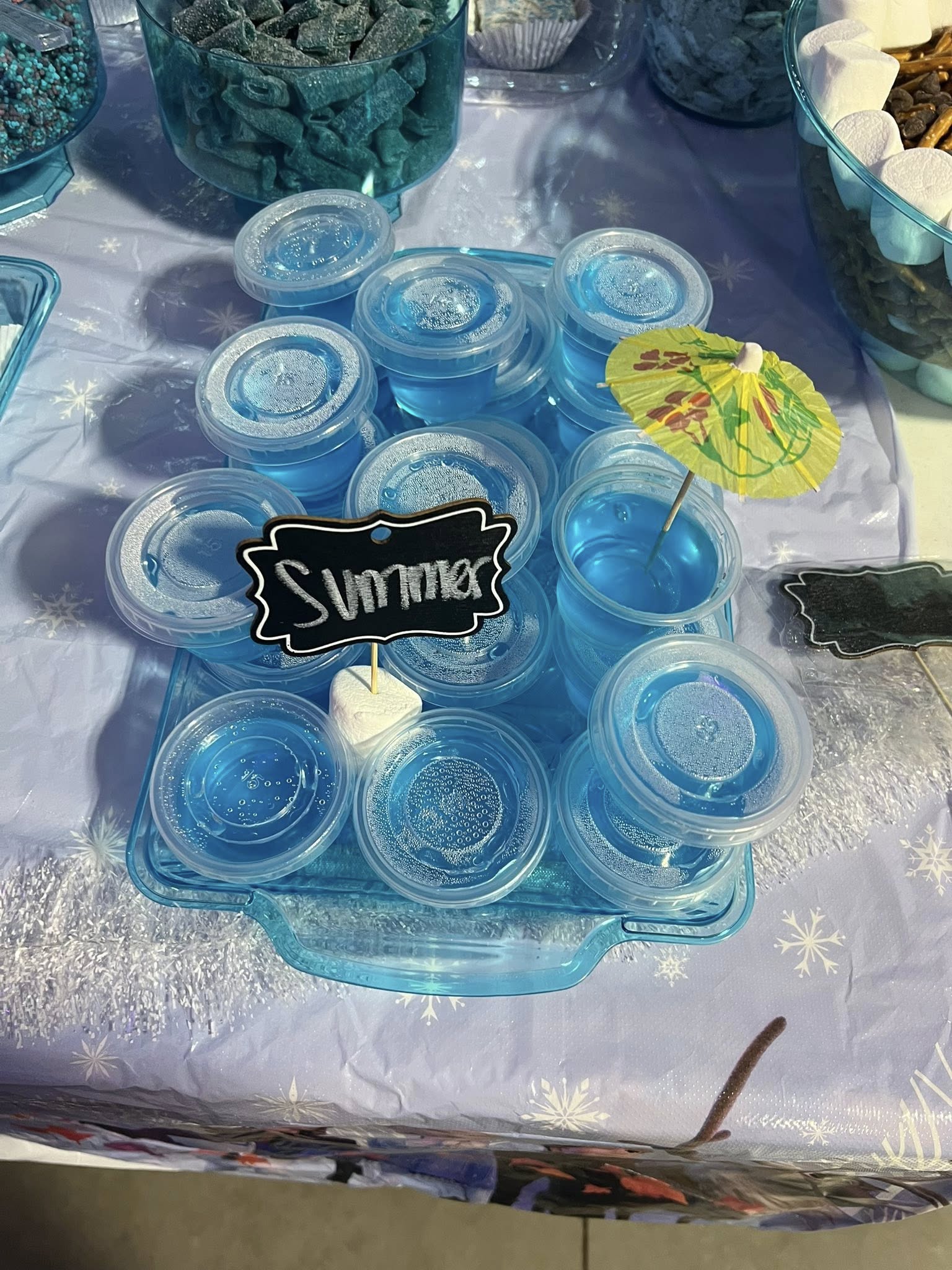 Tray of individual blue jelly cups labeled Summer, garnished with a tropical paper umbrella.