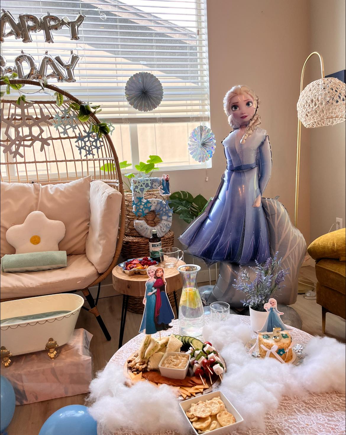 Frozen themed 5th birthday party setup with an Elsa balloon, character cake toppers, and snacks on a table.