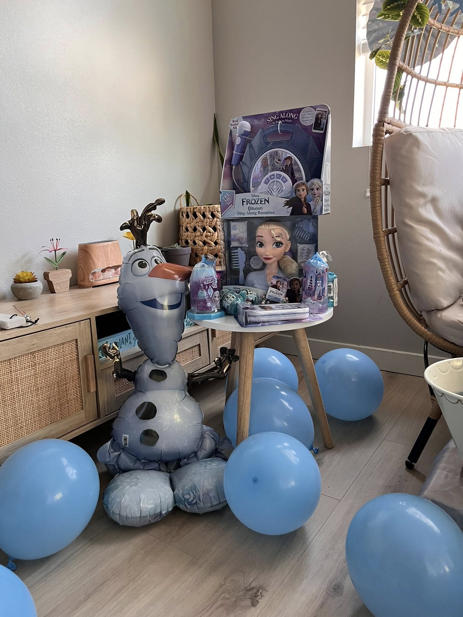 Disney Frozen branded toys, including a sing-along boombox and styling head, displayed on a small table with an Olaf balloon.