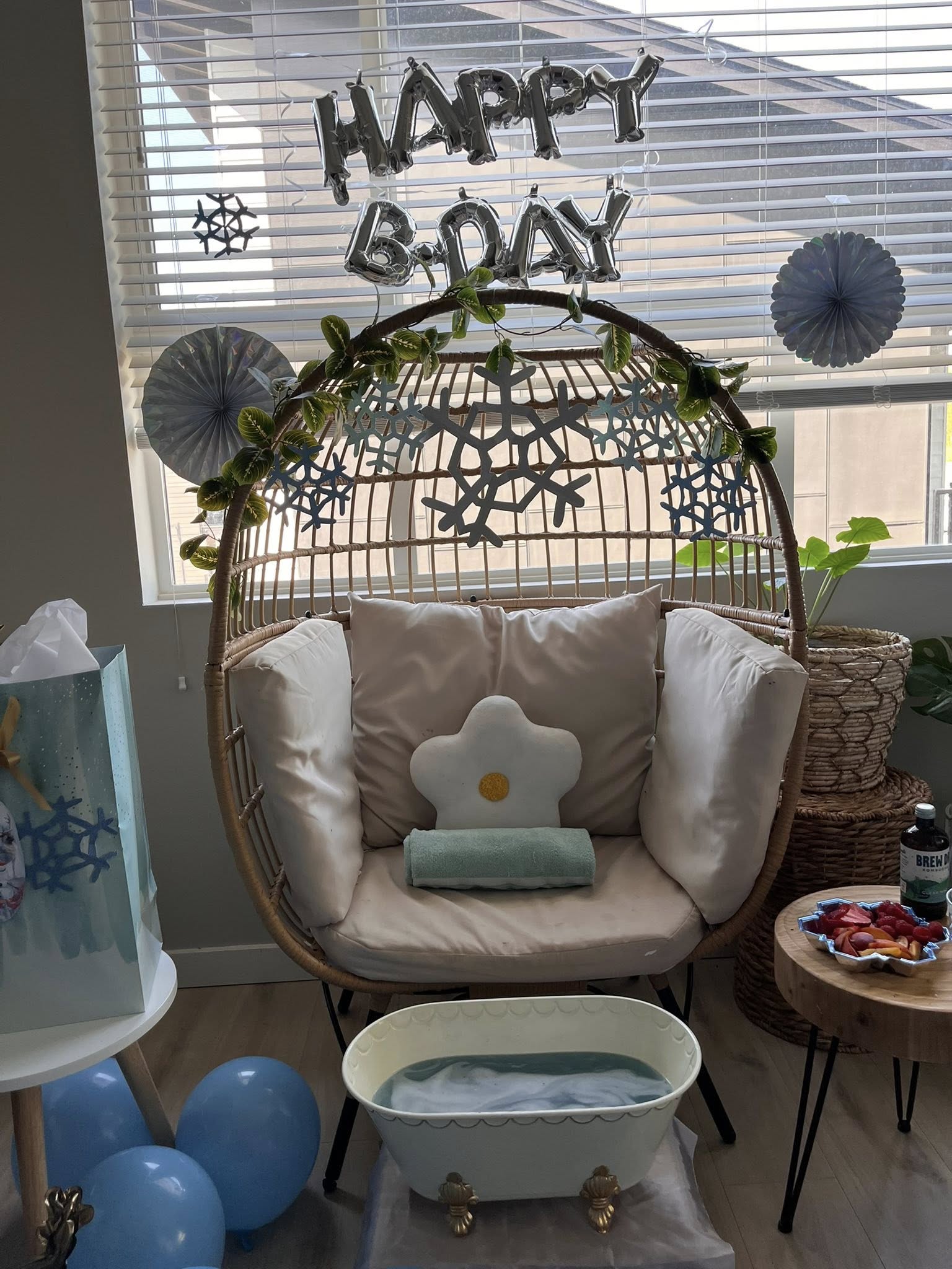 Rattan egg chair decorated with snowflake cutouts and a Happy B-Day balloon sign for an at-home spa birthday.