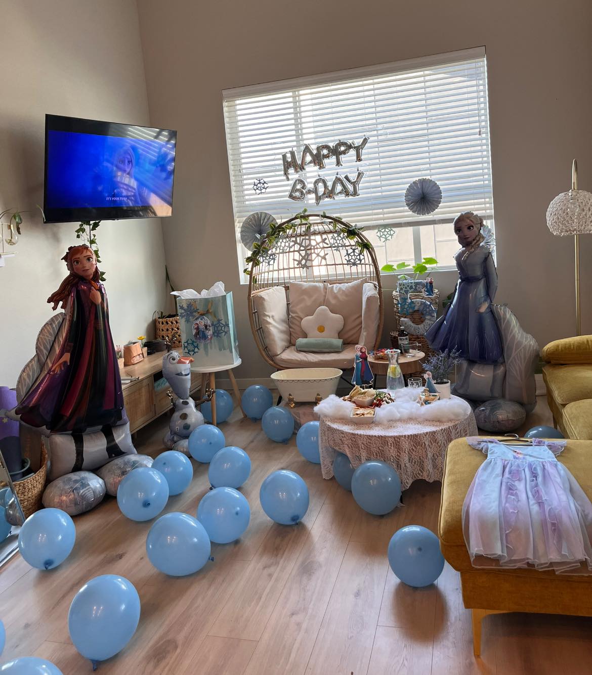 Living room decorated for a Frozen-themed 5th birthday party with blue balloons and character balloons.