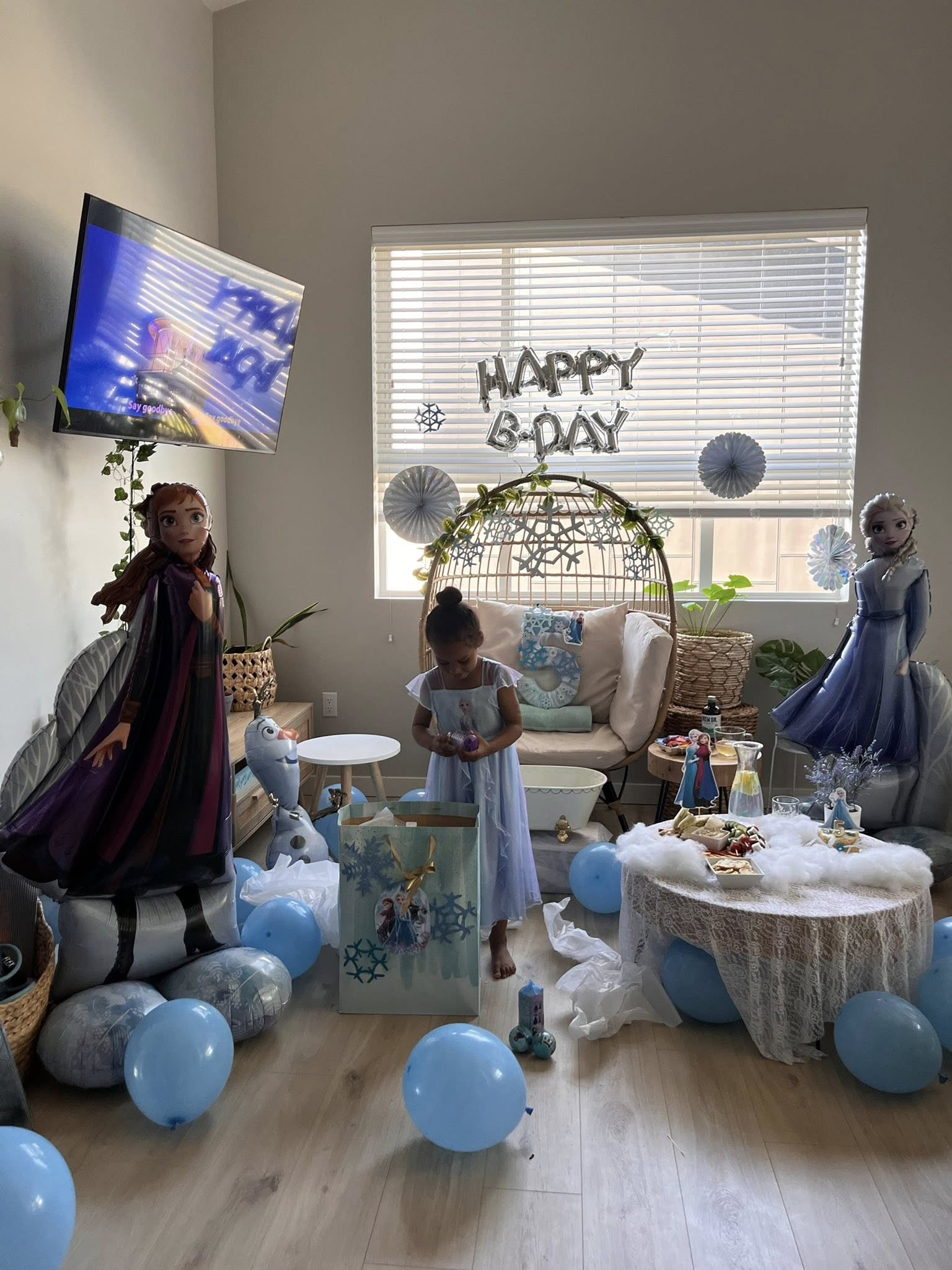 Young girl celebrating her 5th birthday with Frozen themed decorations, balloons of Anna, Elsa, and Olaf.