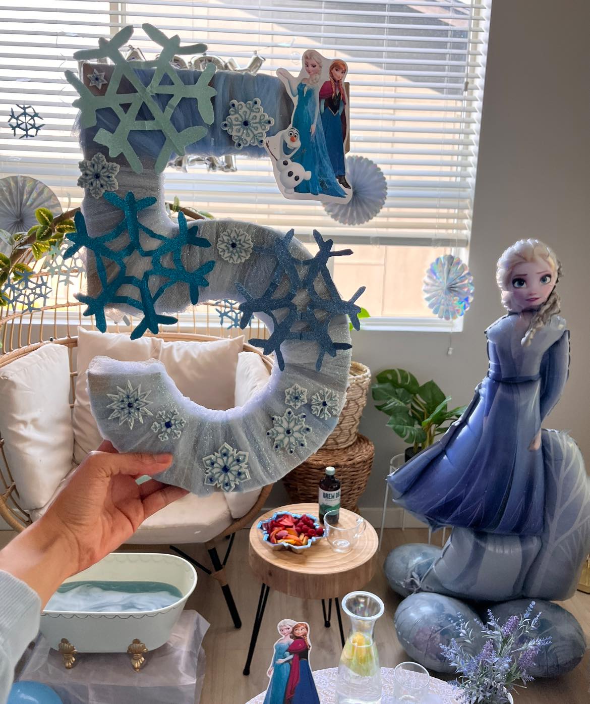 Hand holding a number 5 birthday decoration themed with Frozen characters and glittery snowflakes.