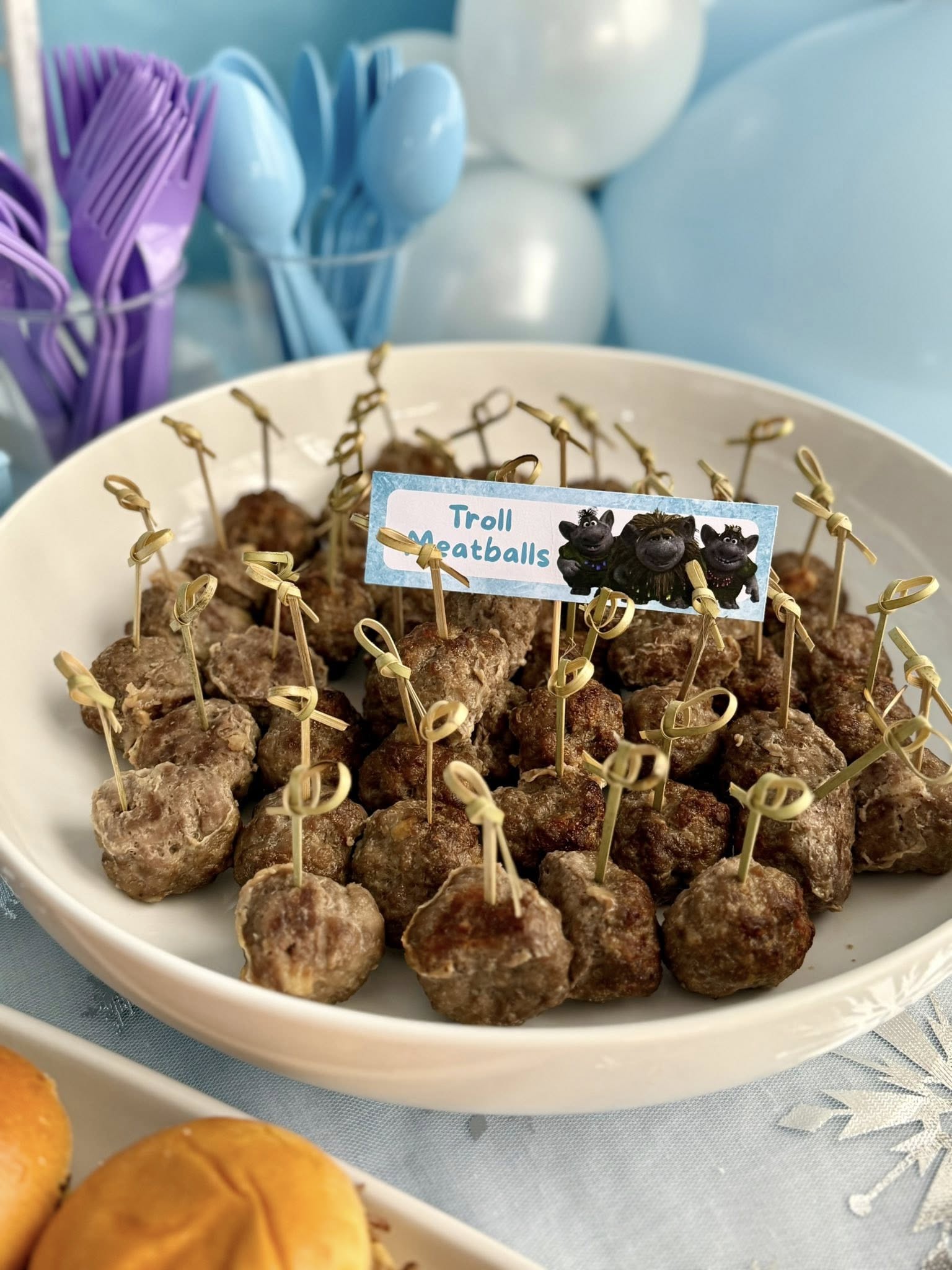 Bowl of cocktail meatballs served on small bamboo skewers with a label that says Troll Meatballs.