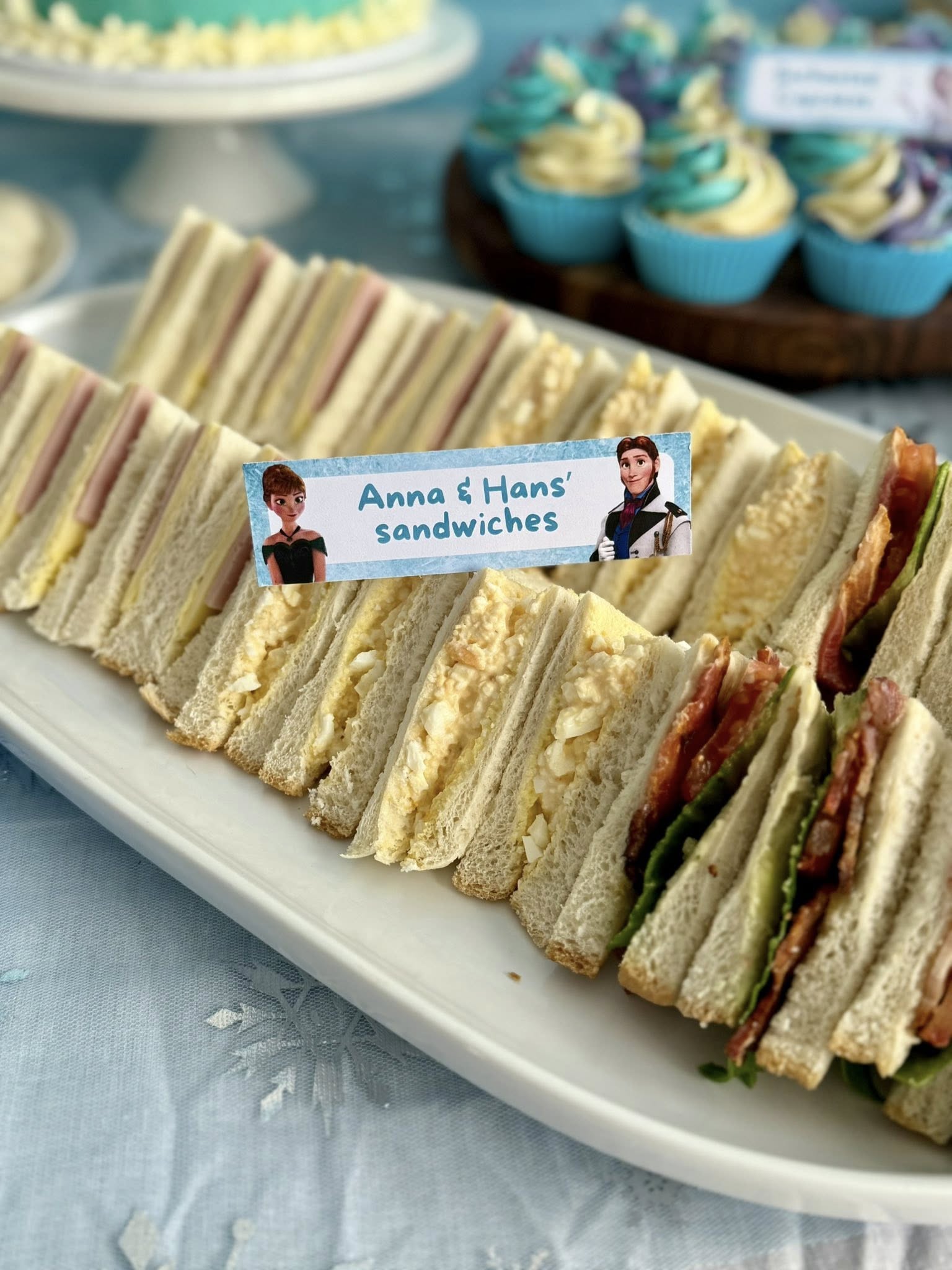 Platter of assorted triangle finger sandwiches labeled as Anna and Hans' sandwiches for a Frozen-themed party.