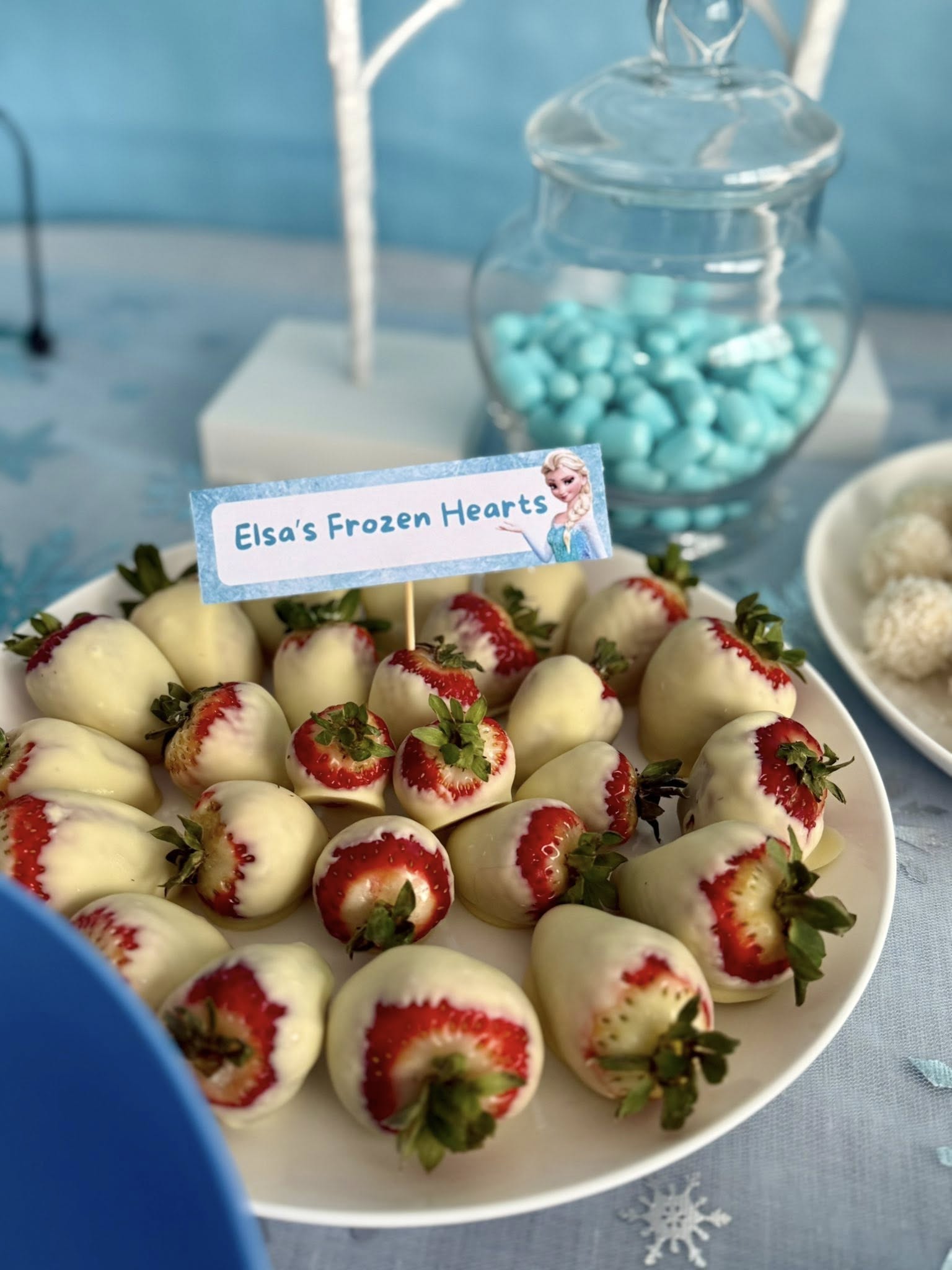 White chocolate-covered strawberries on a plate with a card labeling them Elsa's Frozen Hearts