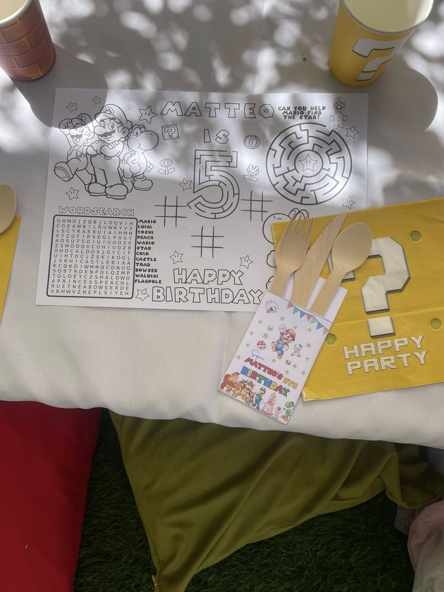 Super Mario themed coloring placemat with word search and 5th birthday design next to wooden cutlery.