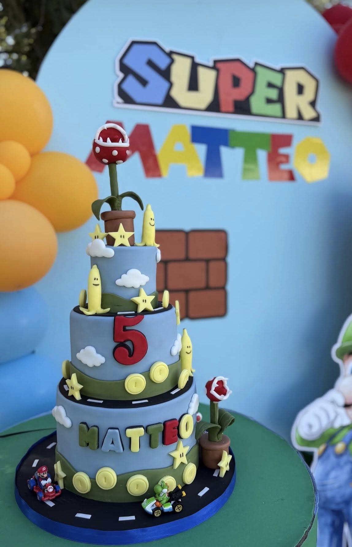 Three-tiered Super Mario themed birthday cake decorated with piranha plants, stars, bananas, and a number five.