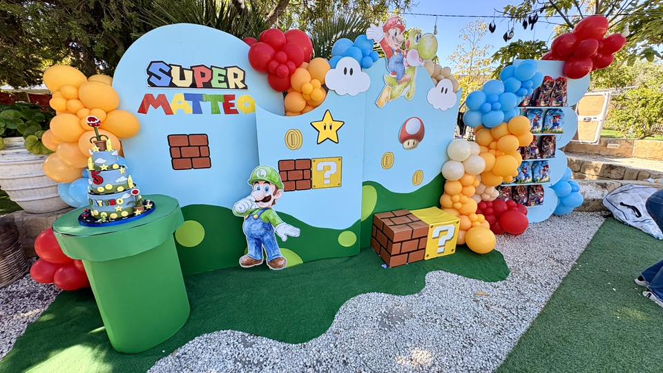 Super Mario themed birthday party setup with balloon arches, a backdrop featuring Luigi, and a tiered cake.