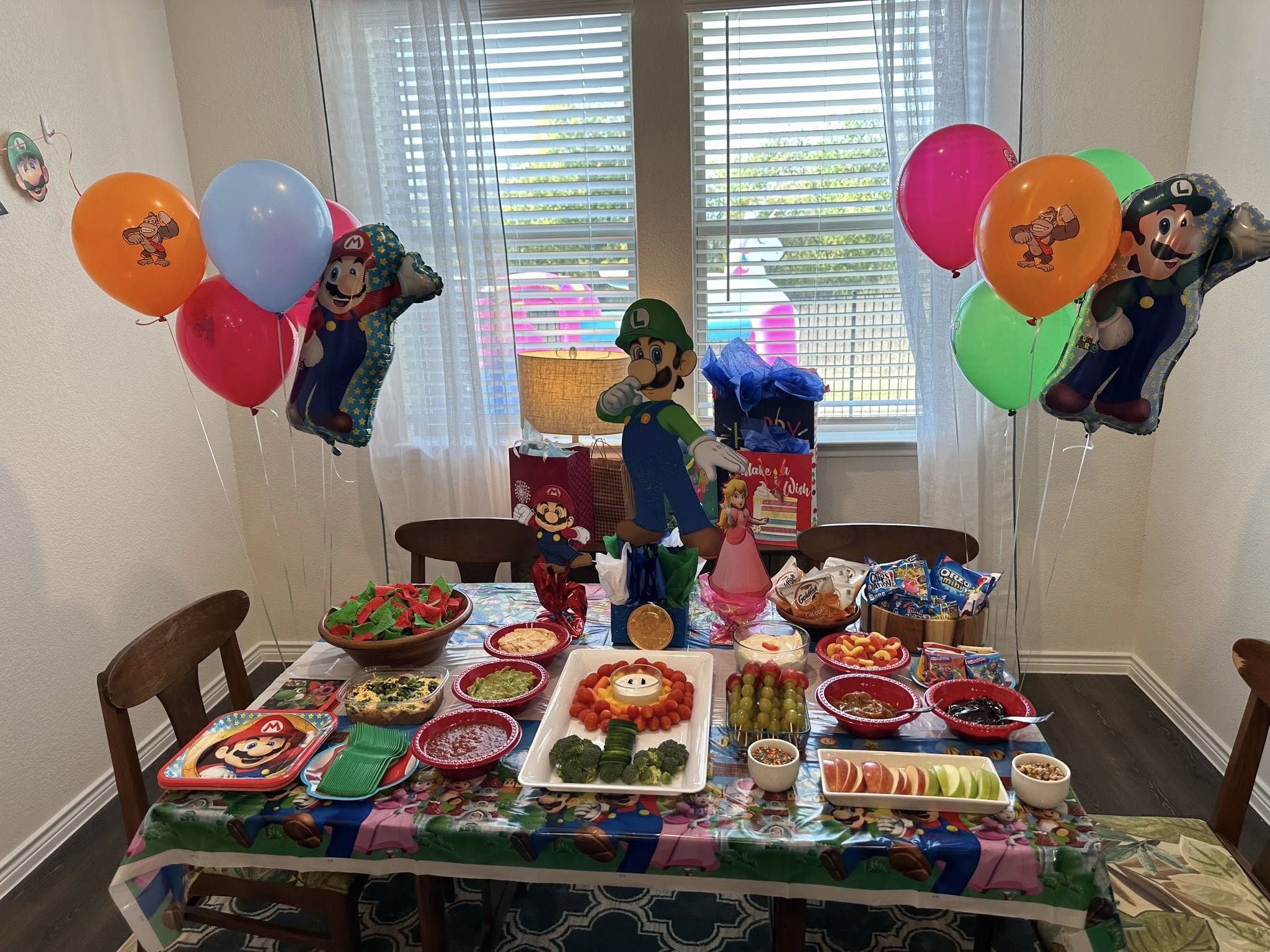Dining table decorated with Super Mario theme party supplies, balloons, and assorted snack bowls for a birthday party.