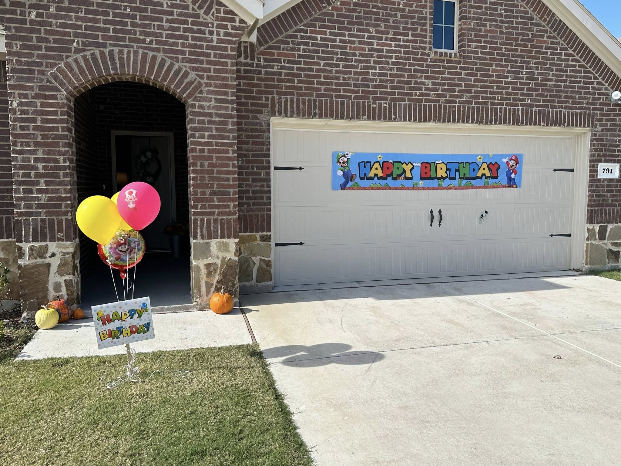 Super Mario themed birthday decorations including a large banner attached to a garage and balloons on the lawn.