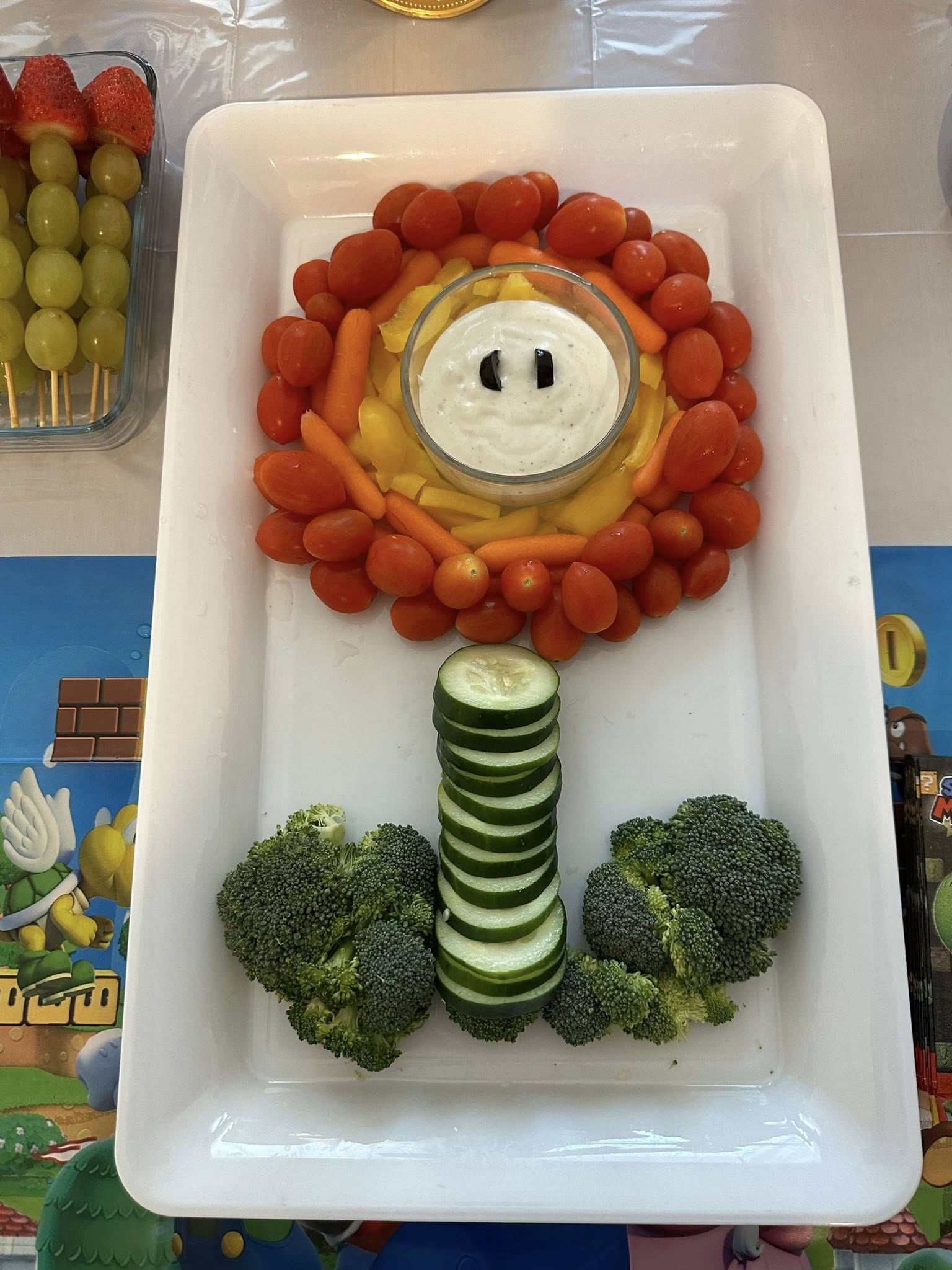 Super Mario Fire Flower vegetable platter with cherry tomatoes, yellow peppers, cucumber, broccoli, and dip.