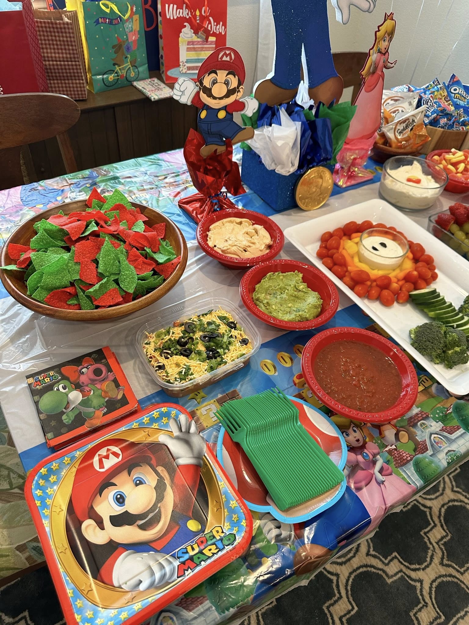 Super Mario themed party table with green and red tortilla chips, dipping sauces, and character-themed tableware.