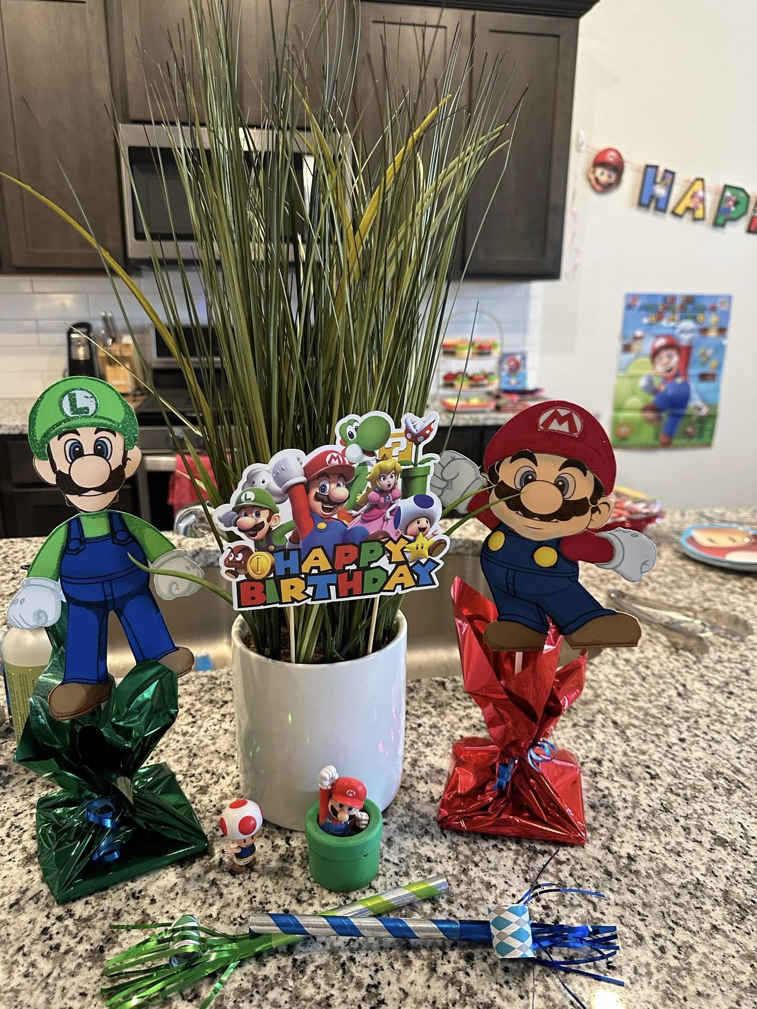 Super Mario themed centerpiece with Luigi and Mario cutouts, a happy birthday sign, and party table decorations.