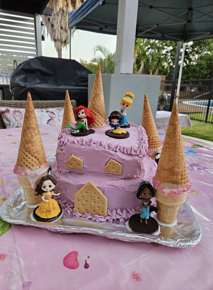 Two-tiered purple castle cake decorated with ice cream cone towers and Disney Princess figurines.