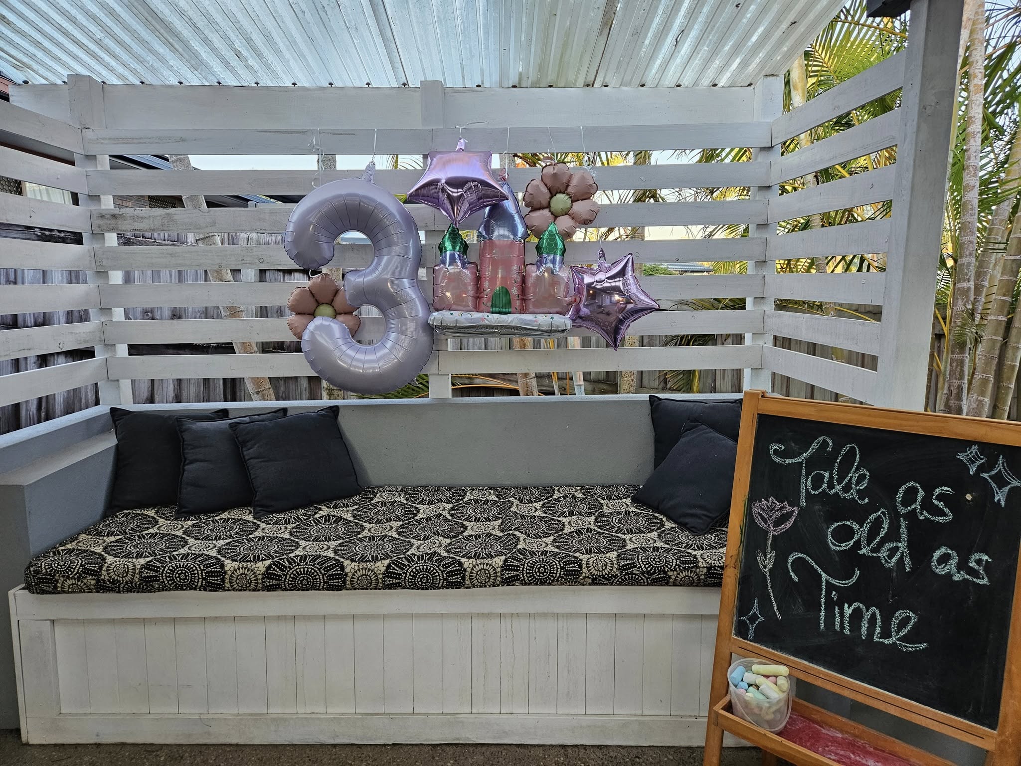 Third birthday party decorations with a princess castle balloon, number 3 balloon, and a chalkboard sign reading Tale as old as Time.