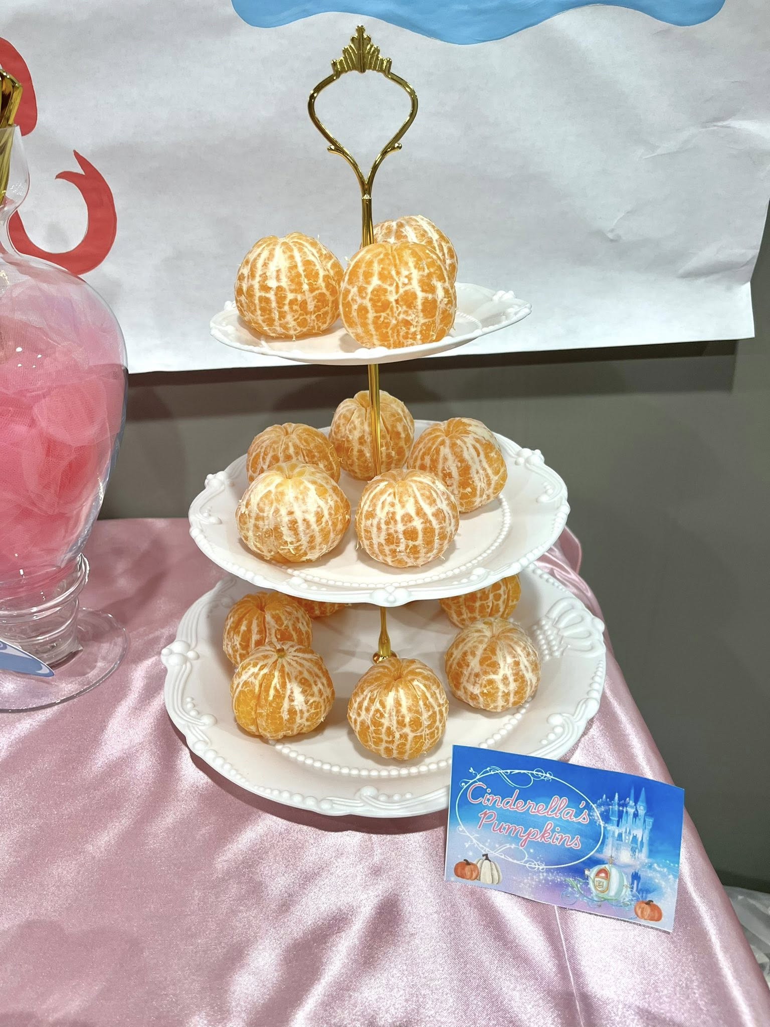 Tiered stand arranged with mandarin oranges labeled as Cinderella's pumpkins for a themed party.