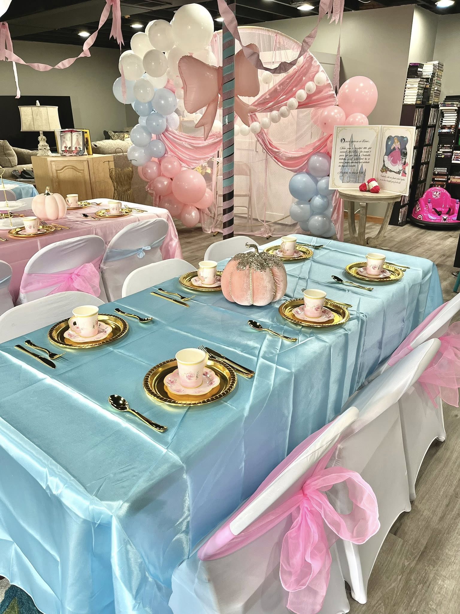 Table set for a princess-themed event with light blue tablecloth, gold plates, floral tea cups, and pink pumpkin centerpiece.