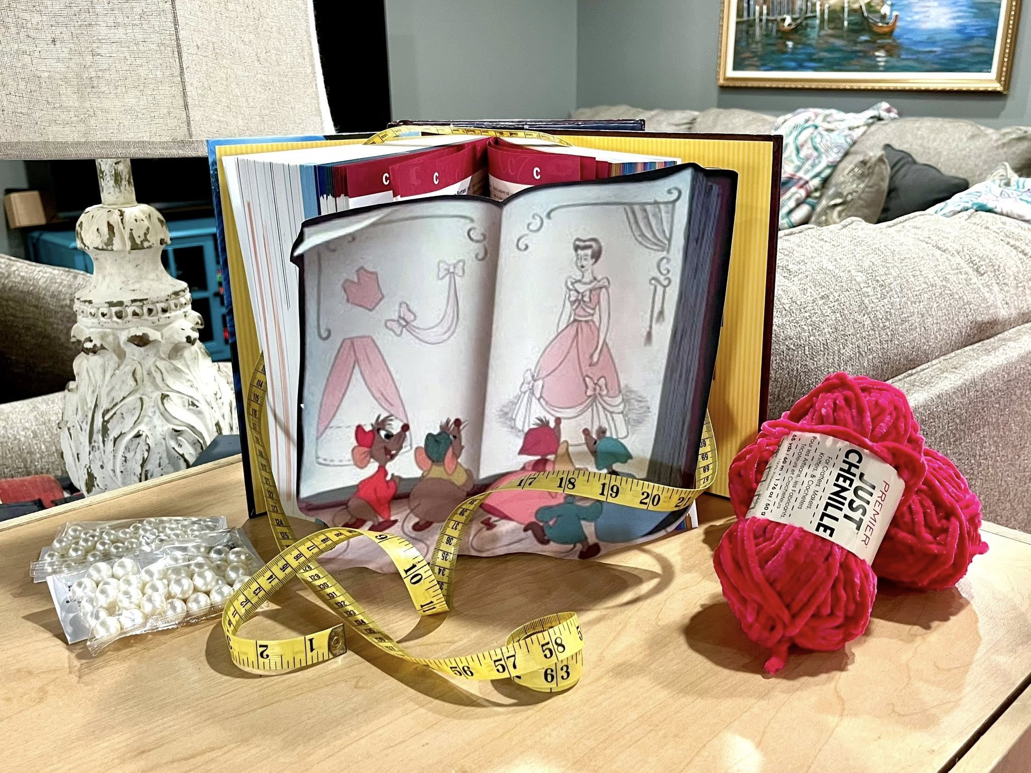 Cinderella storybook illustration surrounded by pink chenille yarn, measuring tape, and a packet of pearls