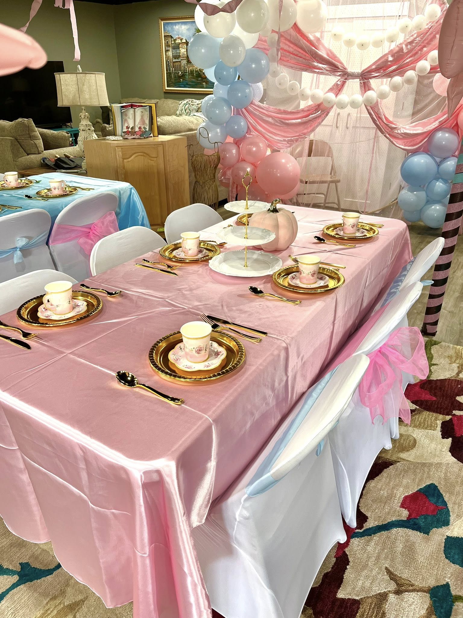 Table set for a party with pink tablecloth, gold-rimmed plates, floral tea cups, and a pastel pink pumpkin centerpiece