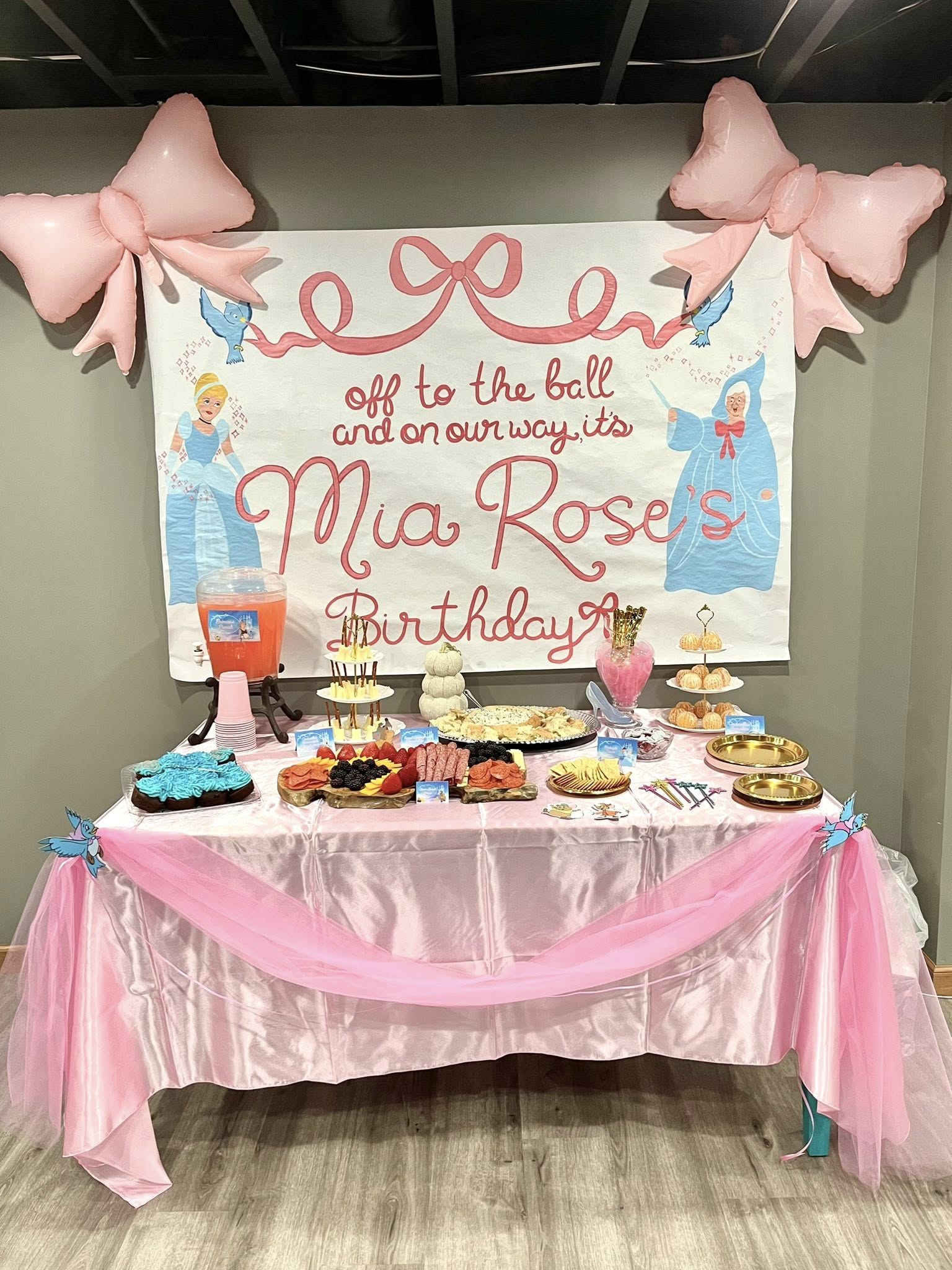 Cinderella themed party dessert table with a personalized pink and white backdrop and bow balloons.