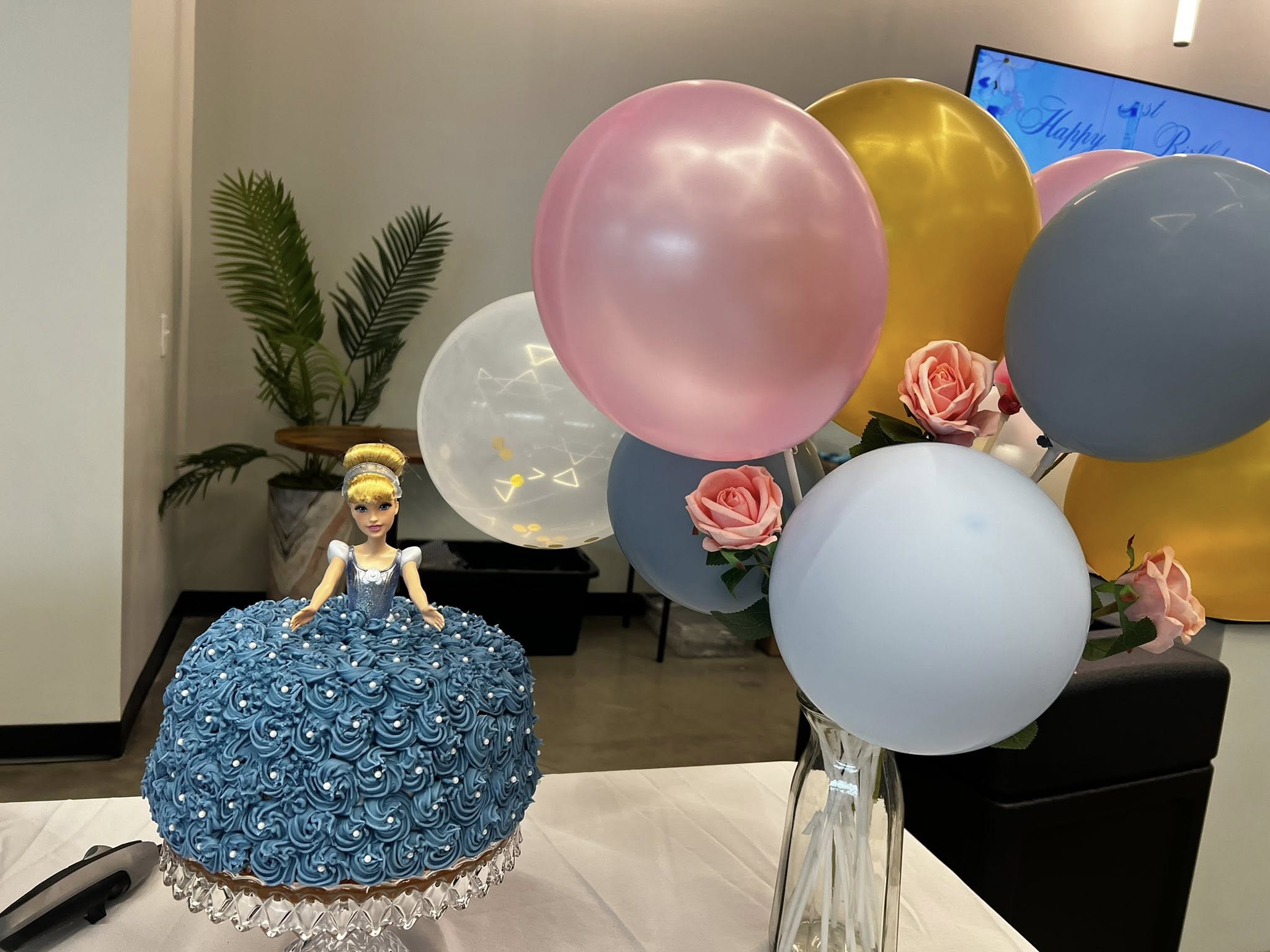 Cinderella doll cake with blue frosting and rose-accented balloons on a birthday party table.