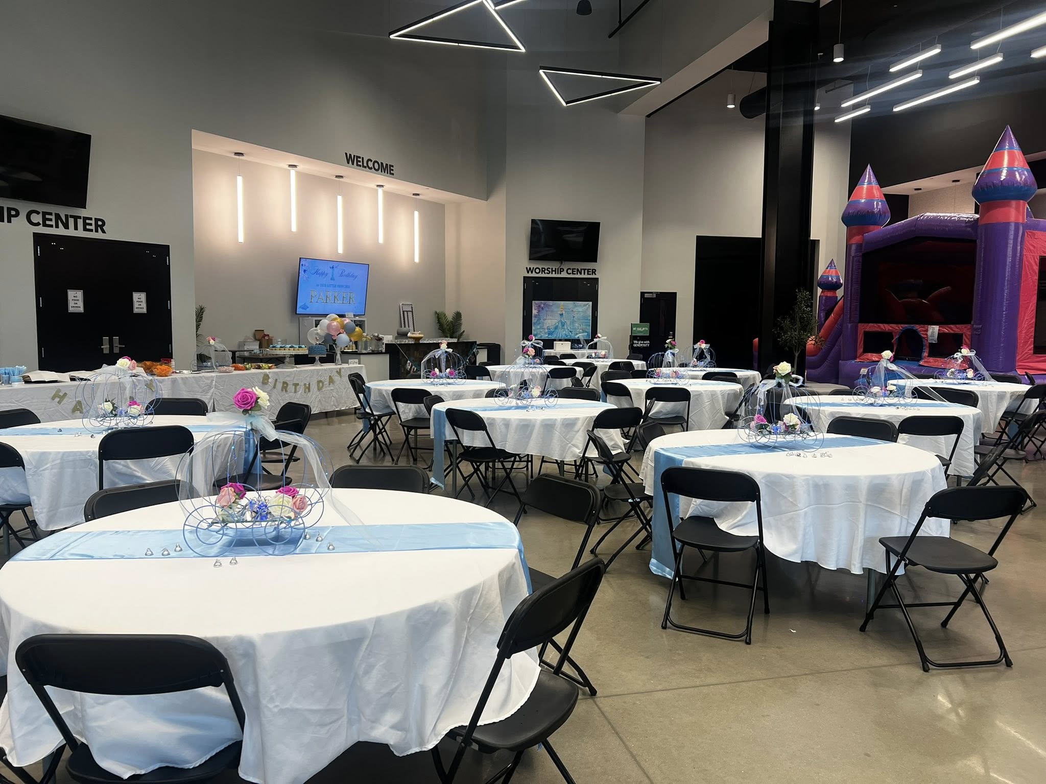 Event space set up for a children's birthday party with tables, light blue runners, carriage centerpieces, and an inflatable bounce house.