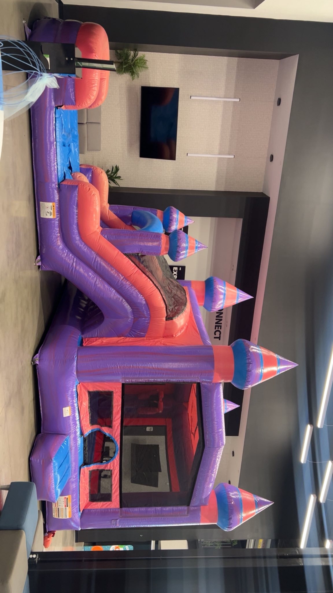 Purple and pink inflatable bounce house castle with a slide set up indoors.