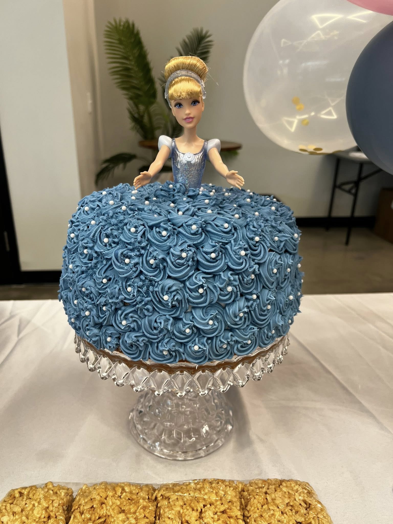 Cinderella doll cake with blue rosette frosting on a glass pedestal stand.