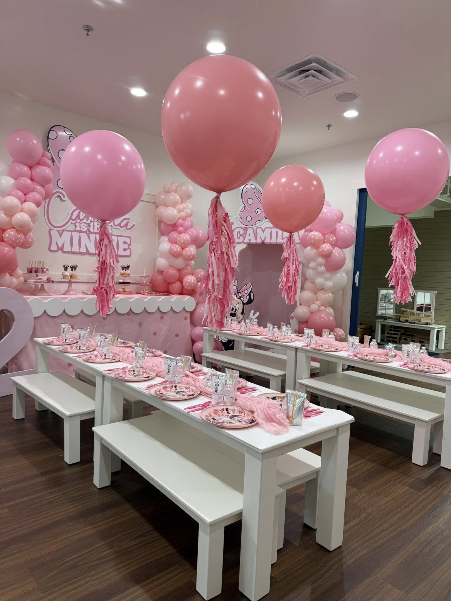 Minnie Mouse themed birthday party setup with pink balloons, white tables, and Minnie-themed plates and decor.