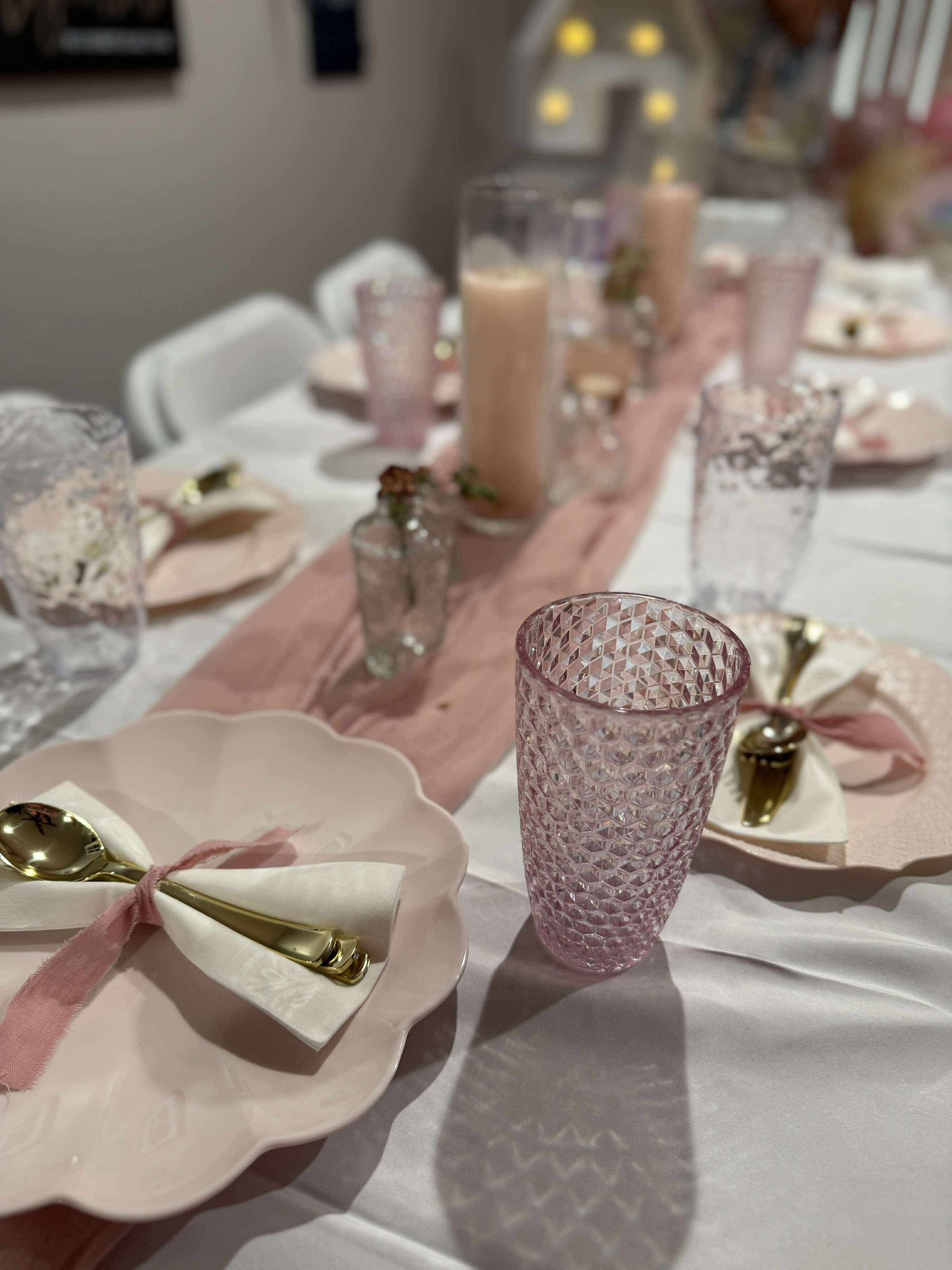 Elegant table setting with pink scalloped plates, textured glassware, gold cutlery, and blush ribbon accents.