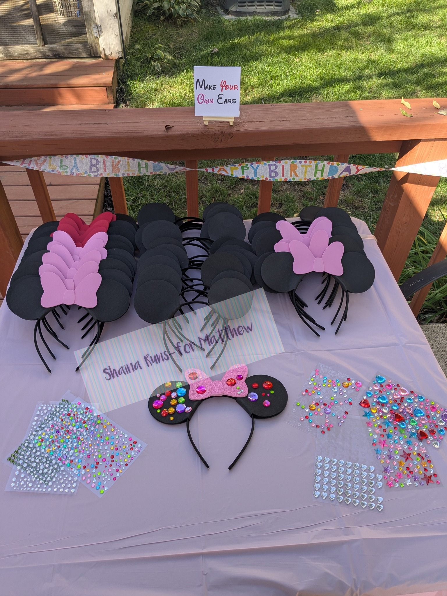 DIY mouse ear crafting station for a birthday party with blank headbands, pink bows, and adhesive gems.