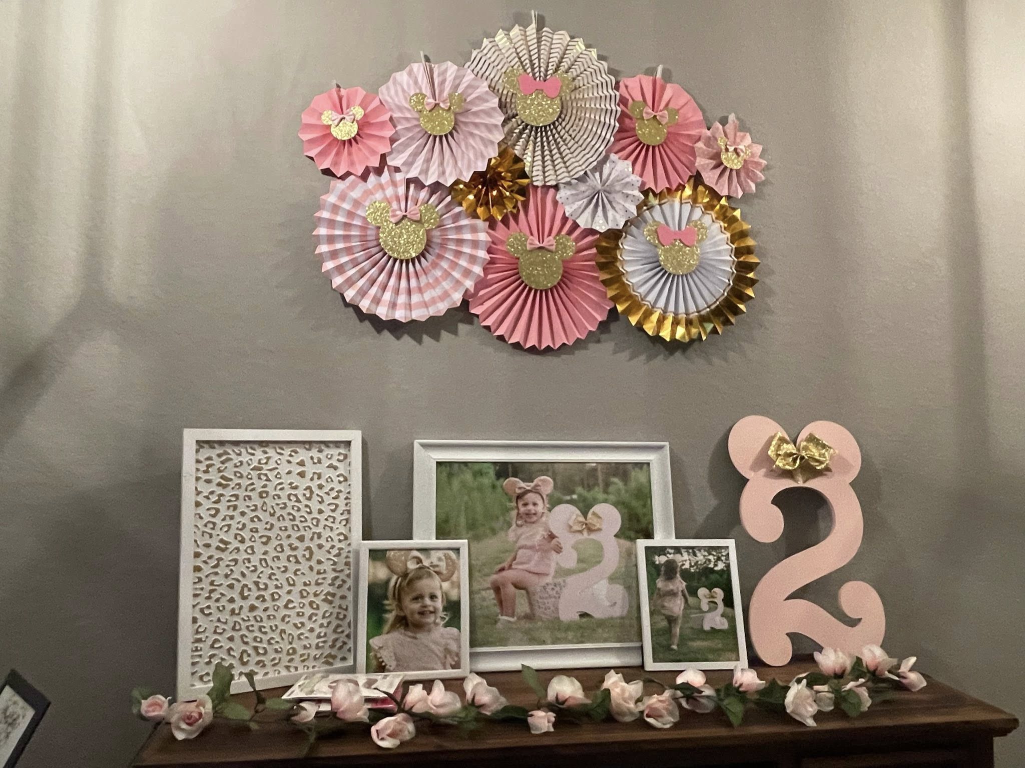 Minnie Mouse themed birthday mantle decor with hanging paper fans, framed photos of a toddler, and a pink number two.