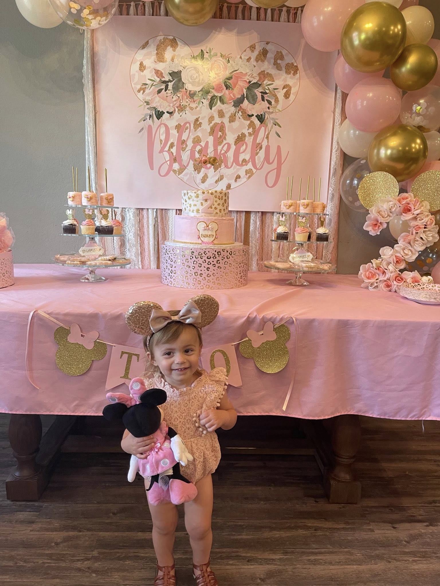 Toddler wearing Minnie Mouse ears in front of a pink and gold leopard print Minnie Mouse-themed birthday table setup