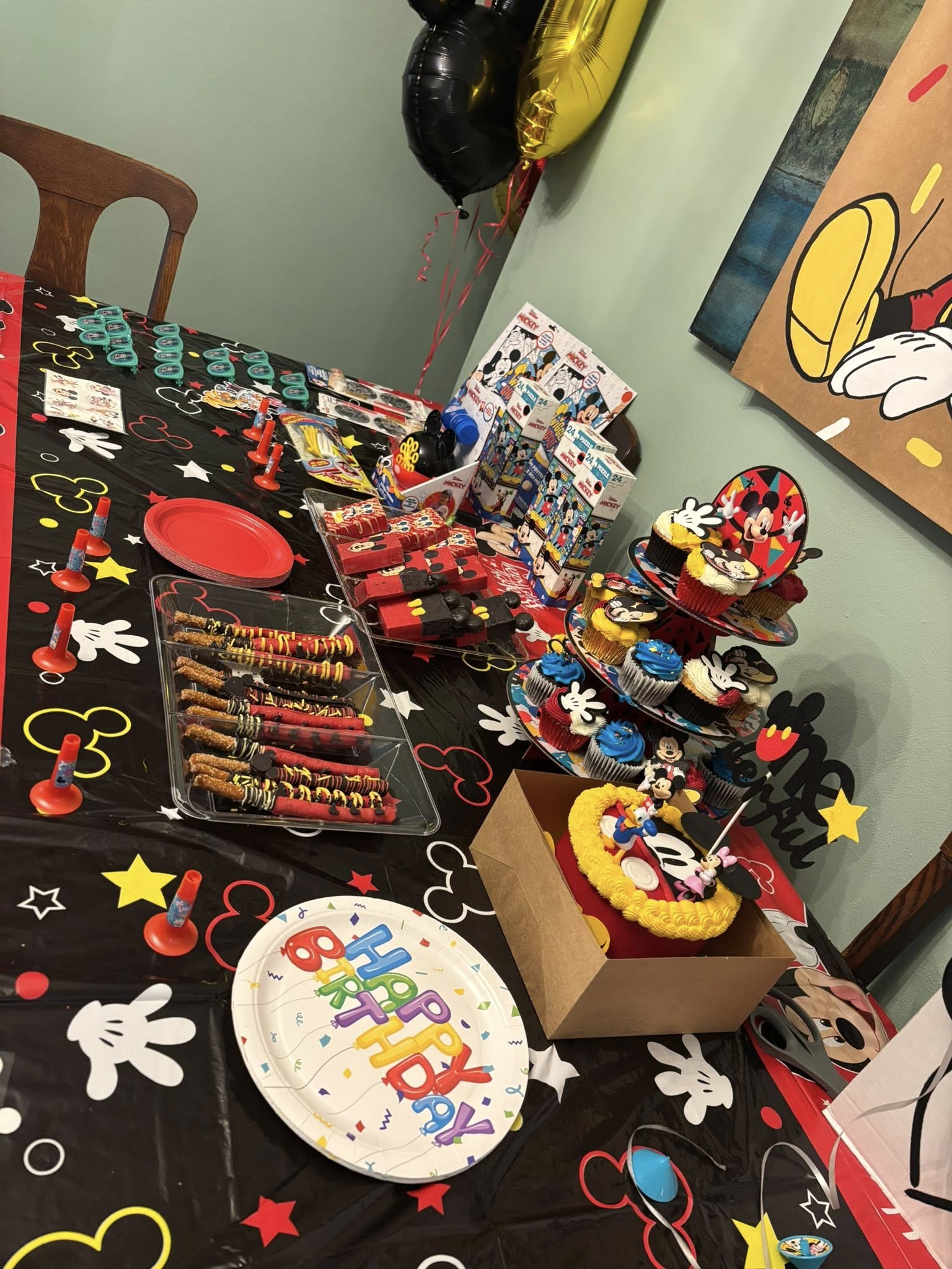 Table decorated with Mickey Mouse themed birthday party supplies, including cupcakes, treats, and snacks.