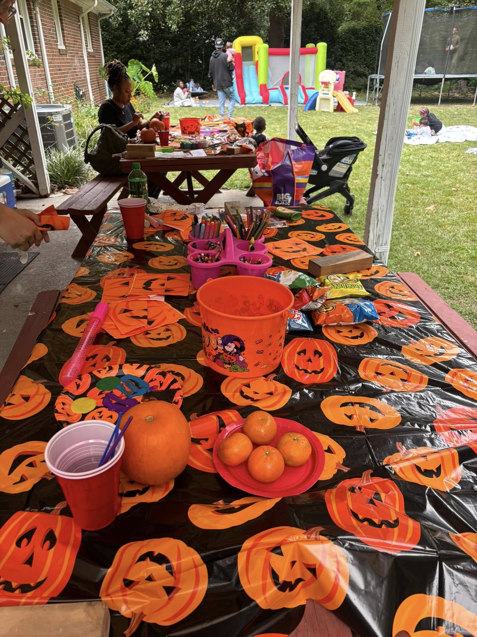 Picnic table decorated with a pumpkin tablecloth, craft supplies, snacks, and fresh tangerines for a Halloween party.