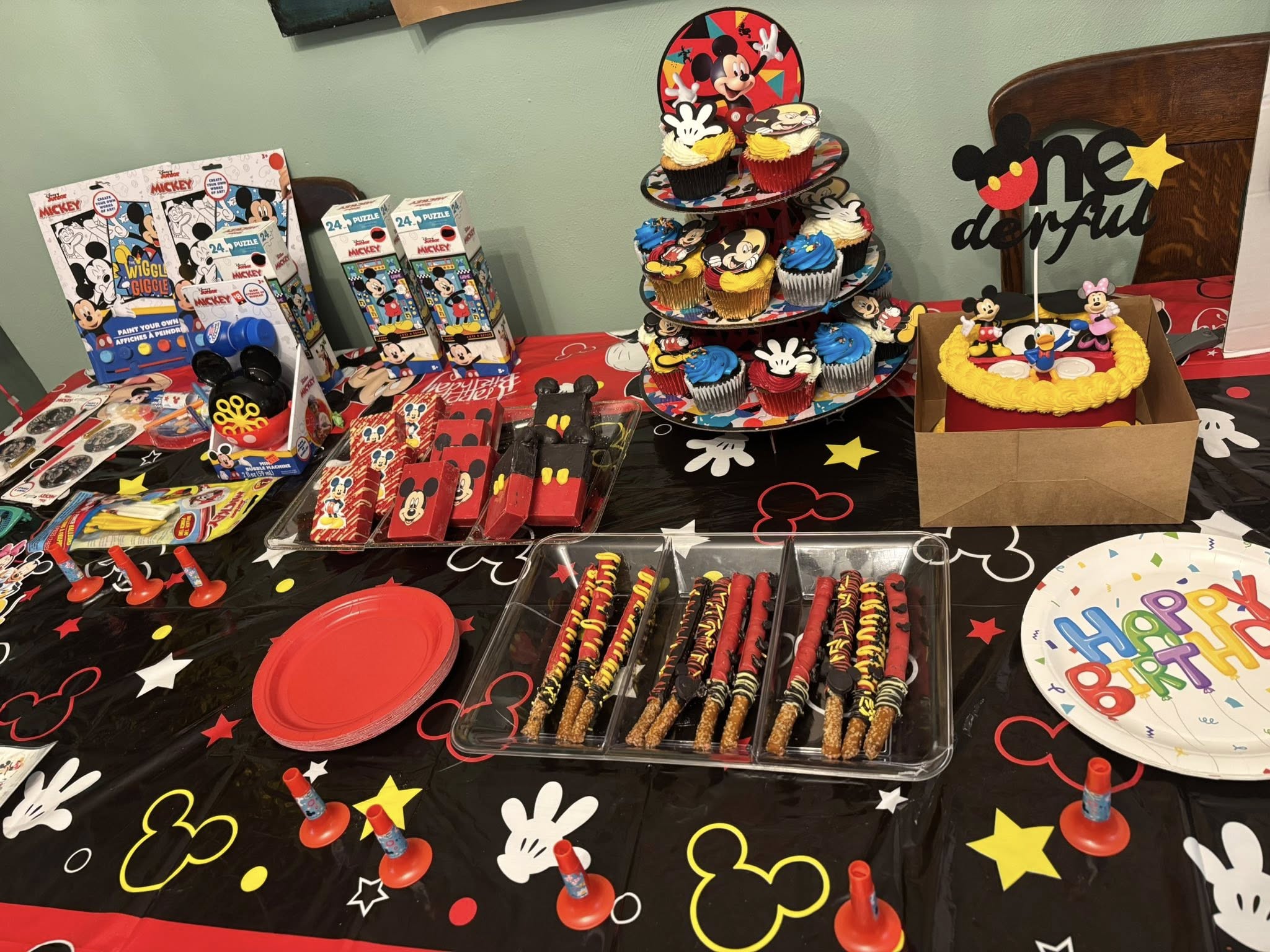 Mickey Mouse themed birthday party table with cupcakes, chocolate-covered pretzels, cake, and party favor boxes.