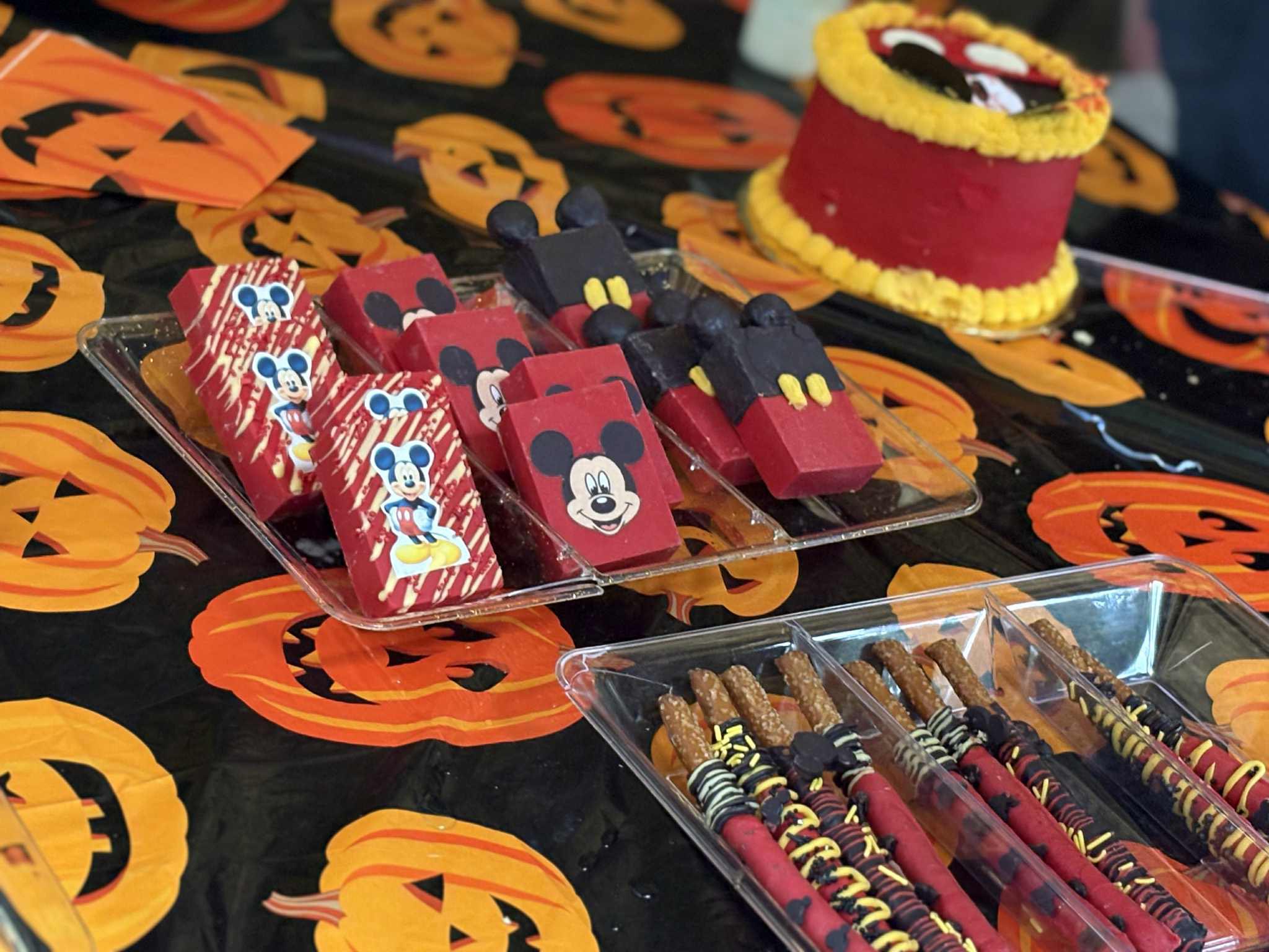Table with Halloween Mickey Mouse themed desserts including decorated brownies and chocolate covered pretzels