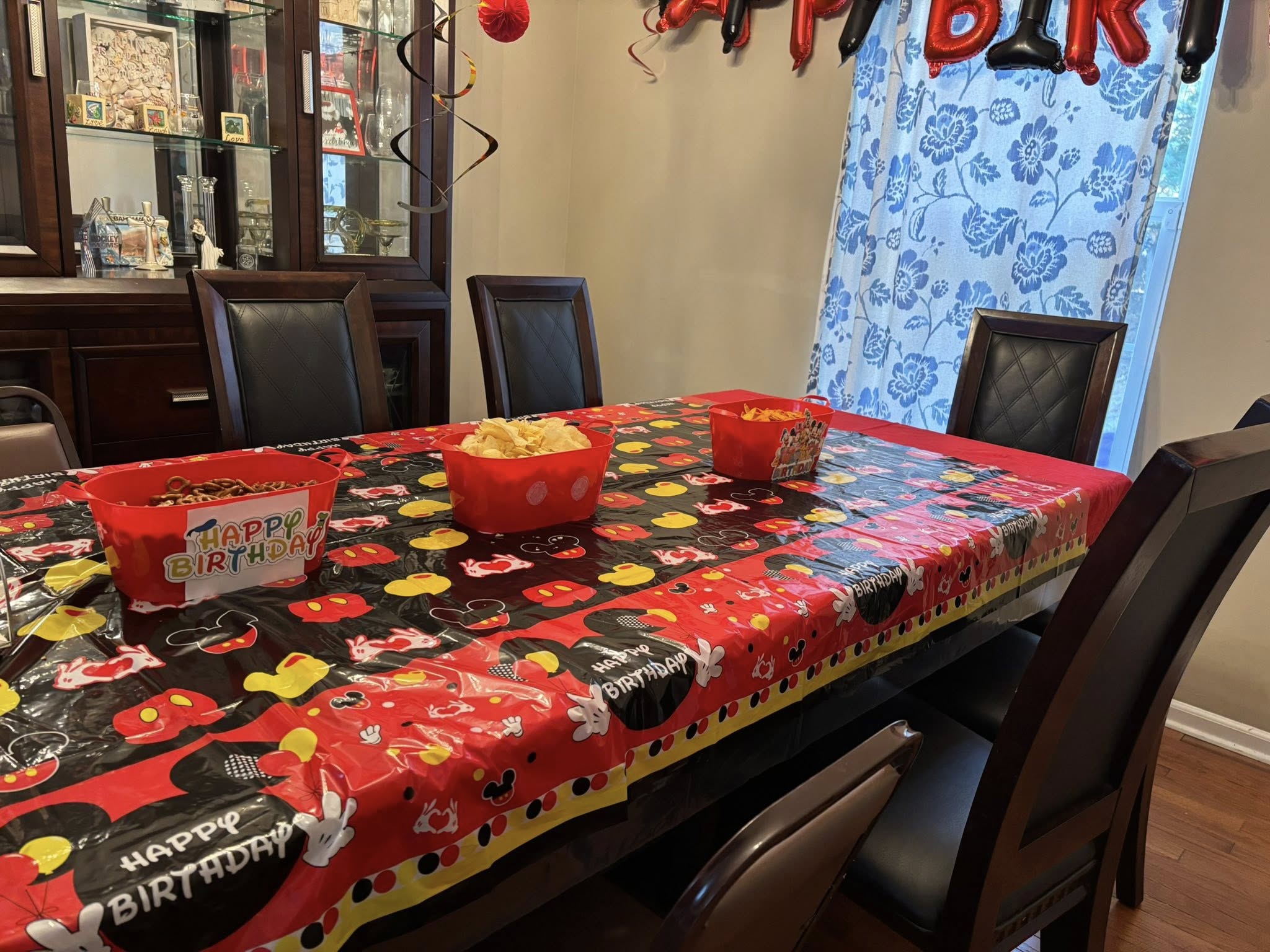 Dining room table set for a Mickey Mouse themed birthday party with plastic Happy Birthday tablecloth and snack bowls.