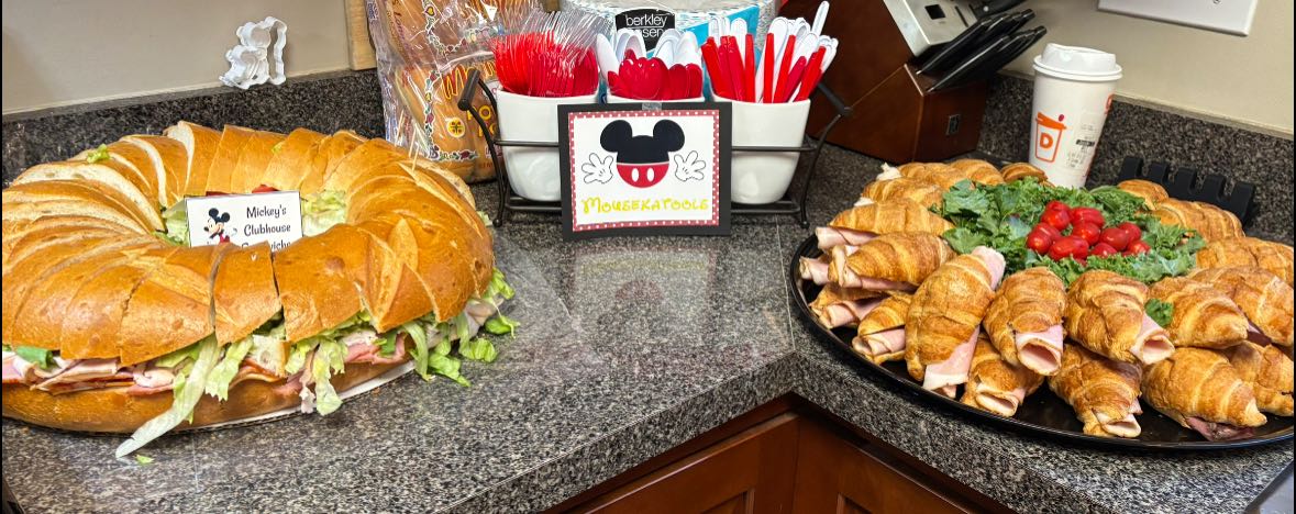Mickey Mouse themed party food display with a large circular sandwich ring and a platter of ham and cheese croissants.