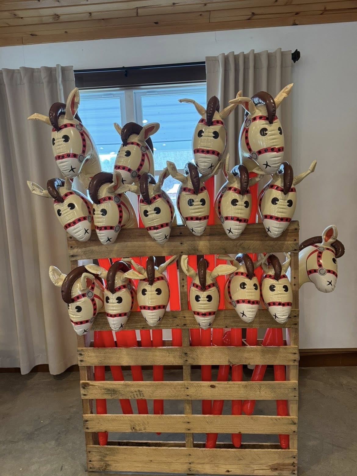 Inflatable stick horse heads mounted on a wooden pallet display.