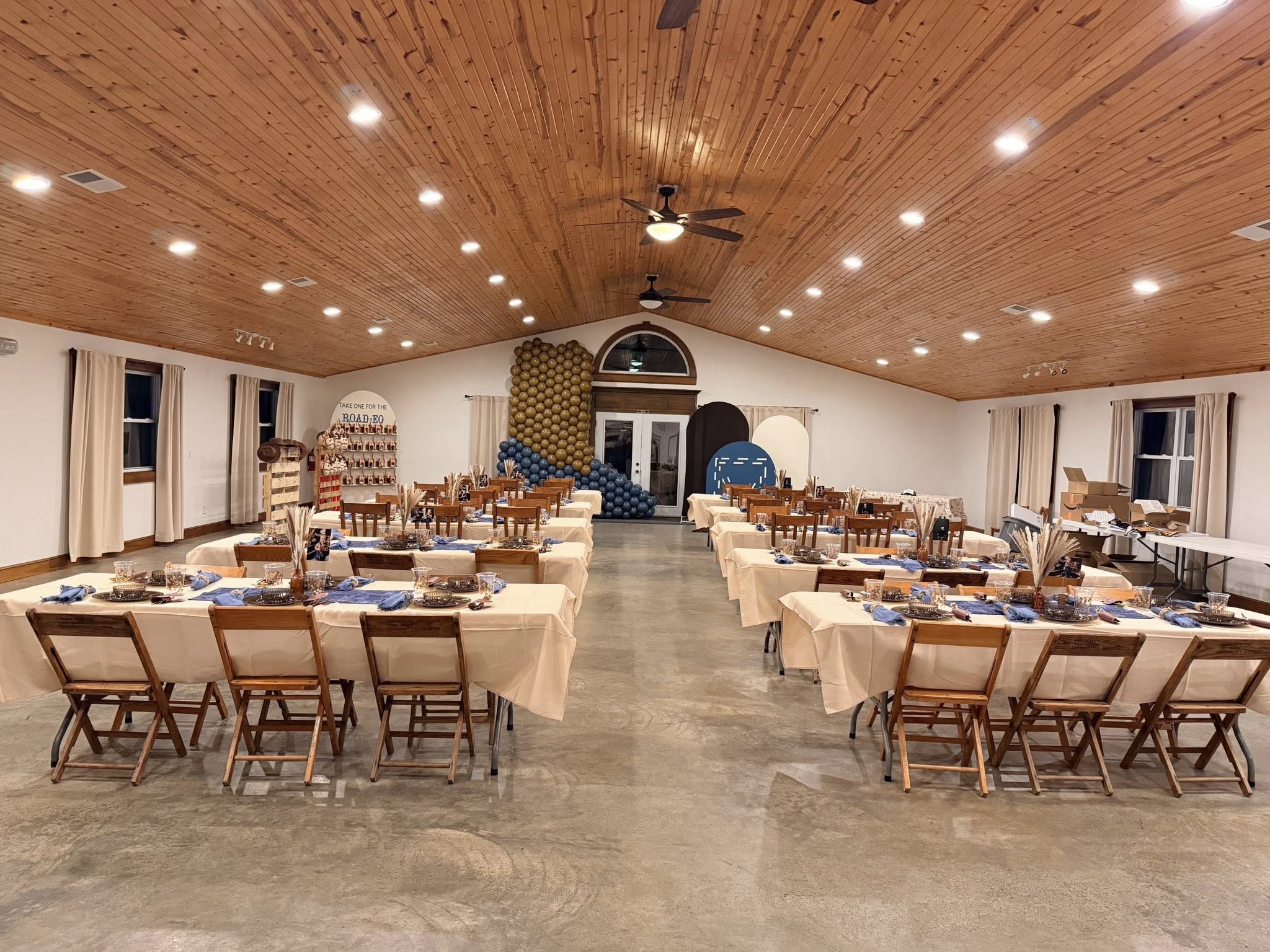 Event venue interior set up with long dining tables, wooden chairs, and rustic rodeo-themed decor.