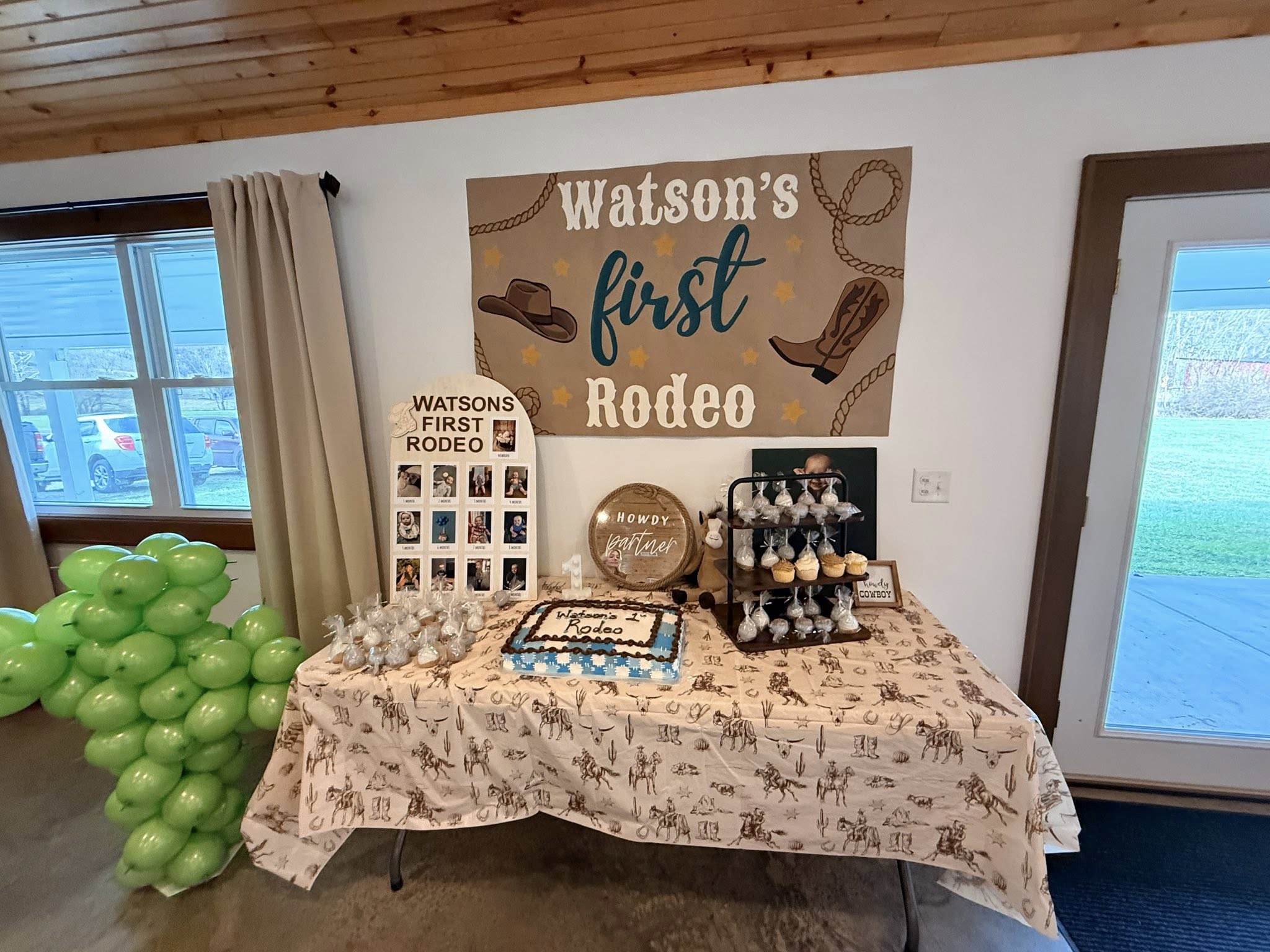 Watson's first rodeo themed party table with a cake, cupcakes, photo display, and green balloon arrangement.
