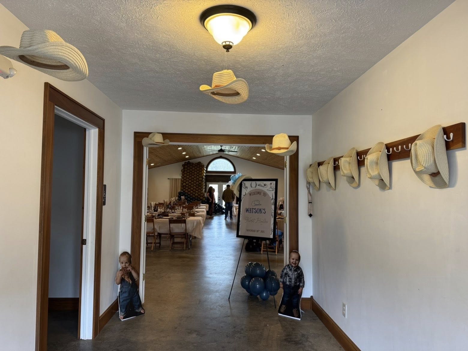 Entryway decorated for a western-themed party with straw hats hung on walls and a Watson's First Rodeo welcome sign.