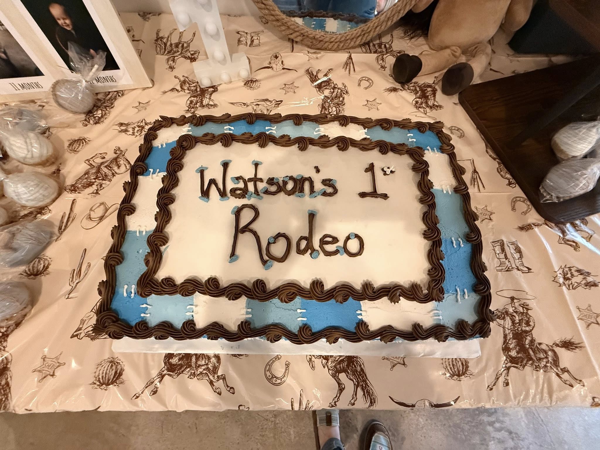 Rectangular sheet cake with Watson's 1st Rodeo written in icing, featuring blue and white checkered border