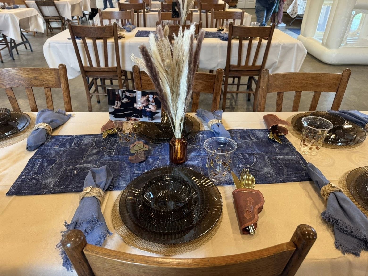 Rustic western themed table setting with denim table runner, pampas grass centerpiece, and copper-toned dinnerware.