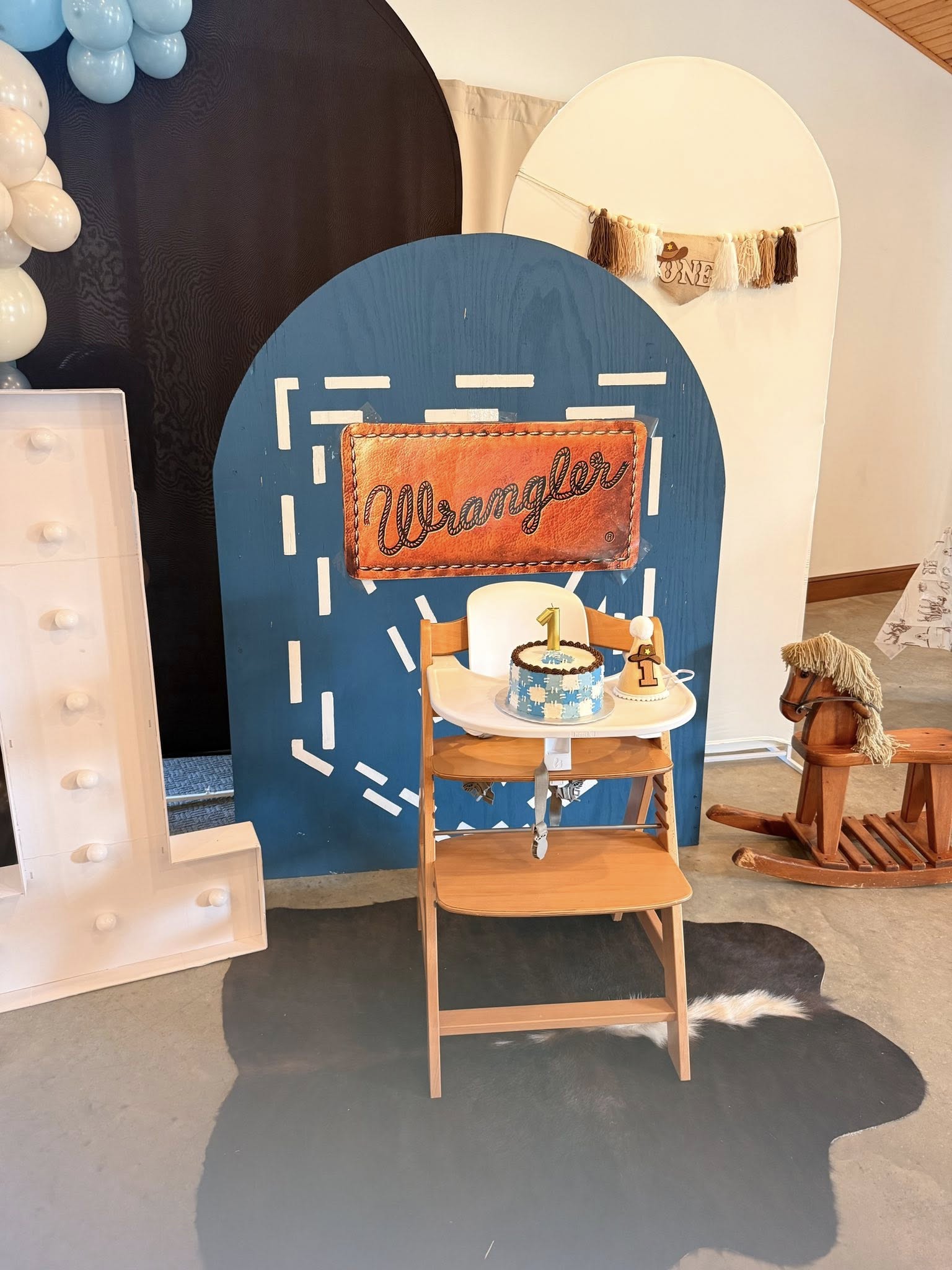 First birthday high chair setup with a Wrangler-themed backdrop, smash cake, and Western decorations.