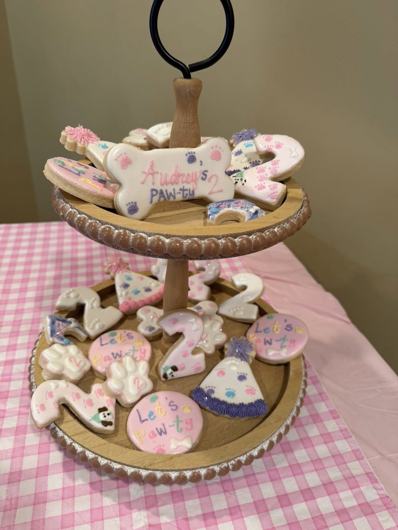 Two-tiered wooden stand filled with custom birthday cookies shaped like bones, paw prints, and the number two.