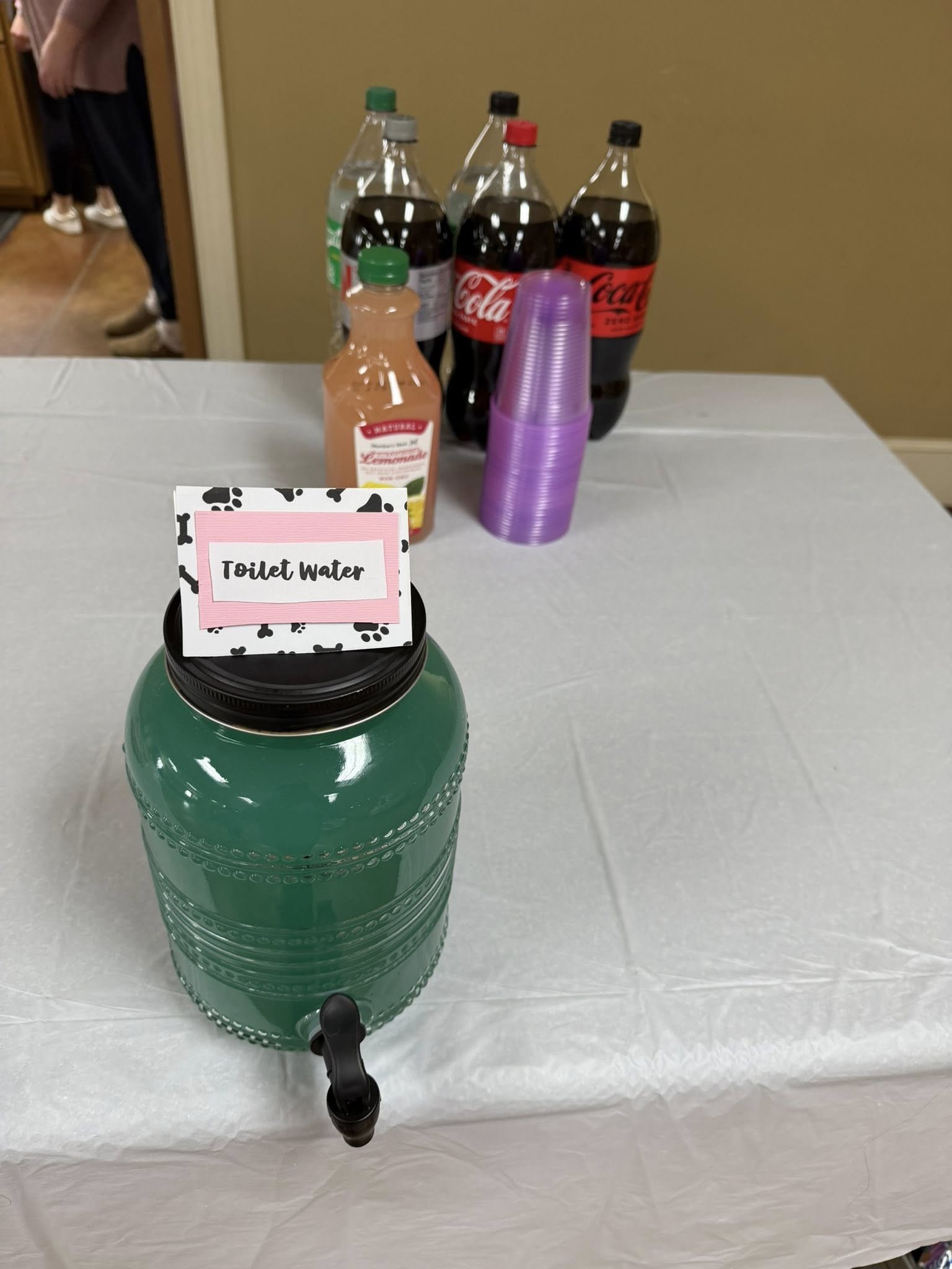 A drink dispenser on a table with a sign labeled Toilet Water.